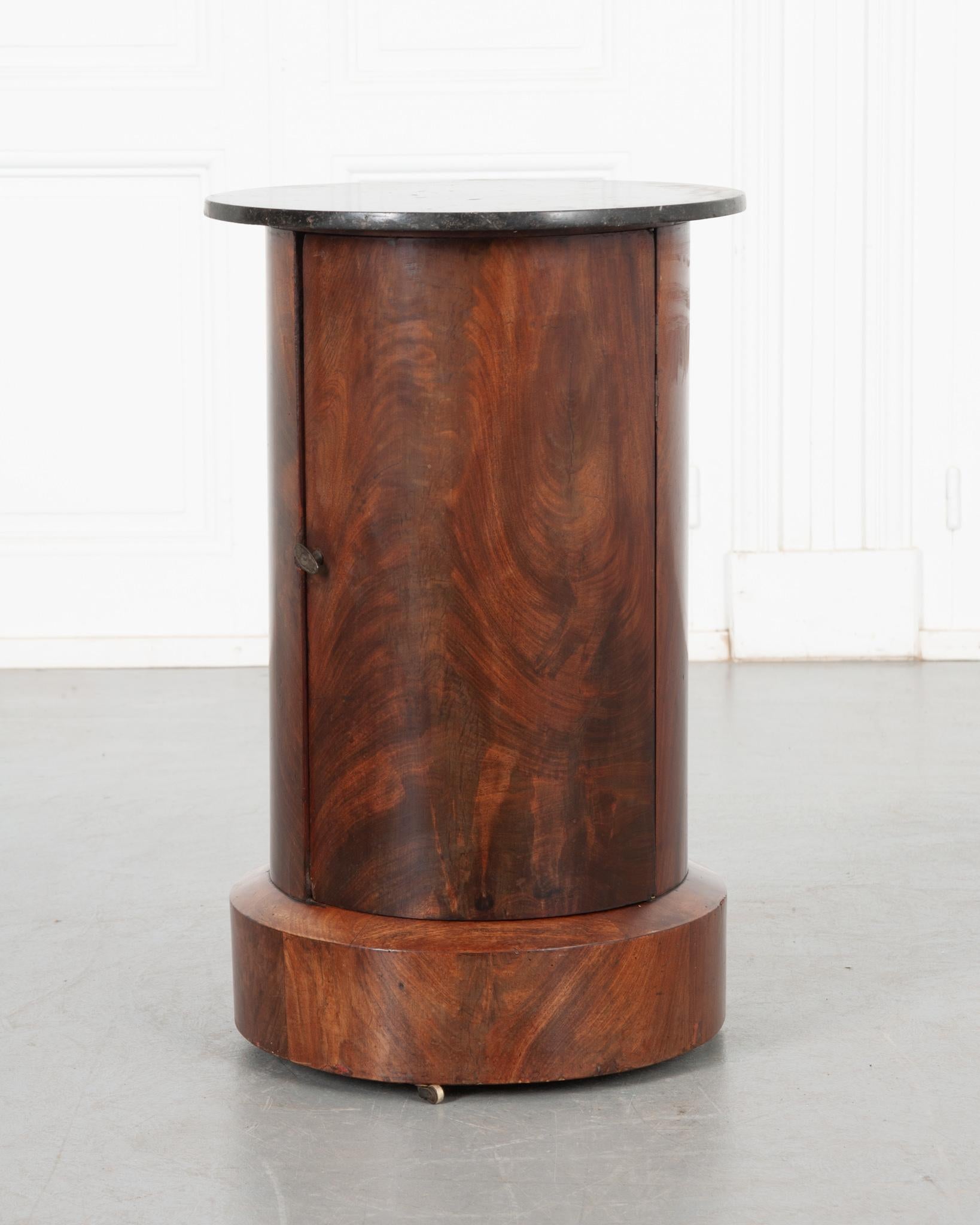 This round column-like piece was crafted in France, circa 1820’s. It has a beautiful fossil black granite top over a solid mahogany body. The door features a neat metal pull that secures the door closed. The interior houses two shelves; one with a