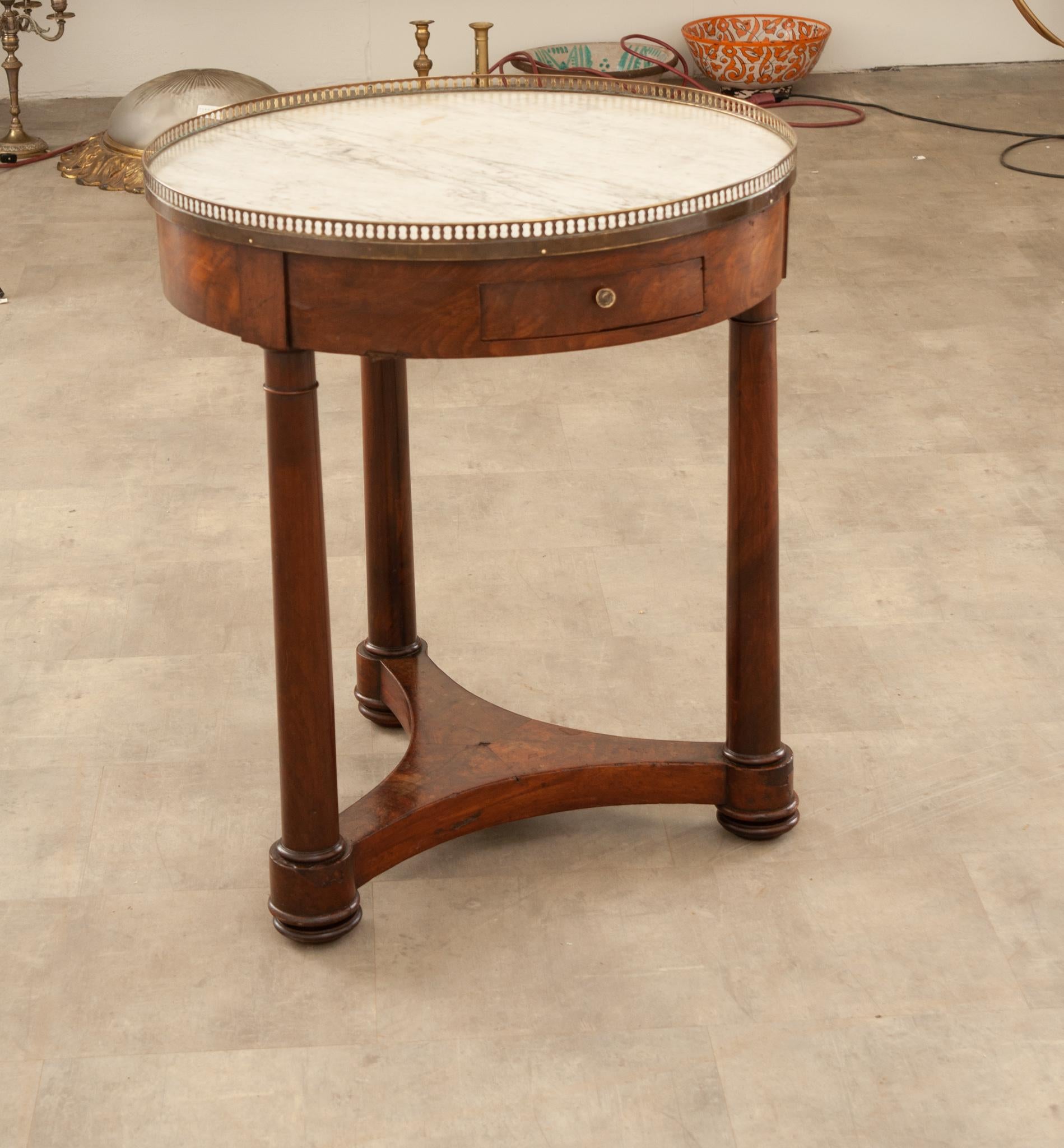 A pierced brass gallery surrounds the round, white marble top on this terrific 19th Century French Empire style gueridon. The top is lifted by three column-form legs that are joined by a concave stretcher below. The apron houses a single drawer