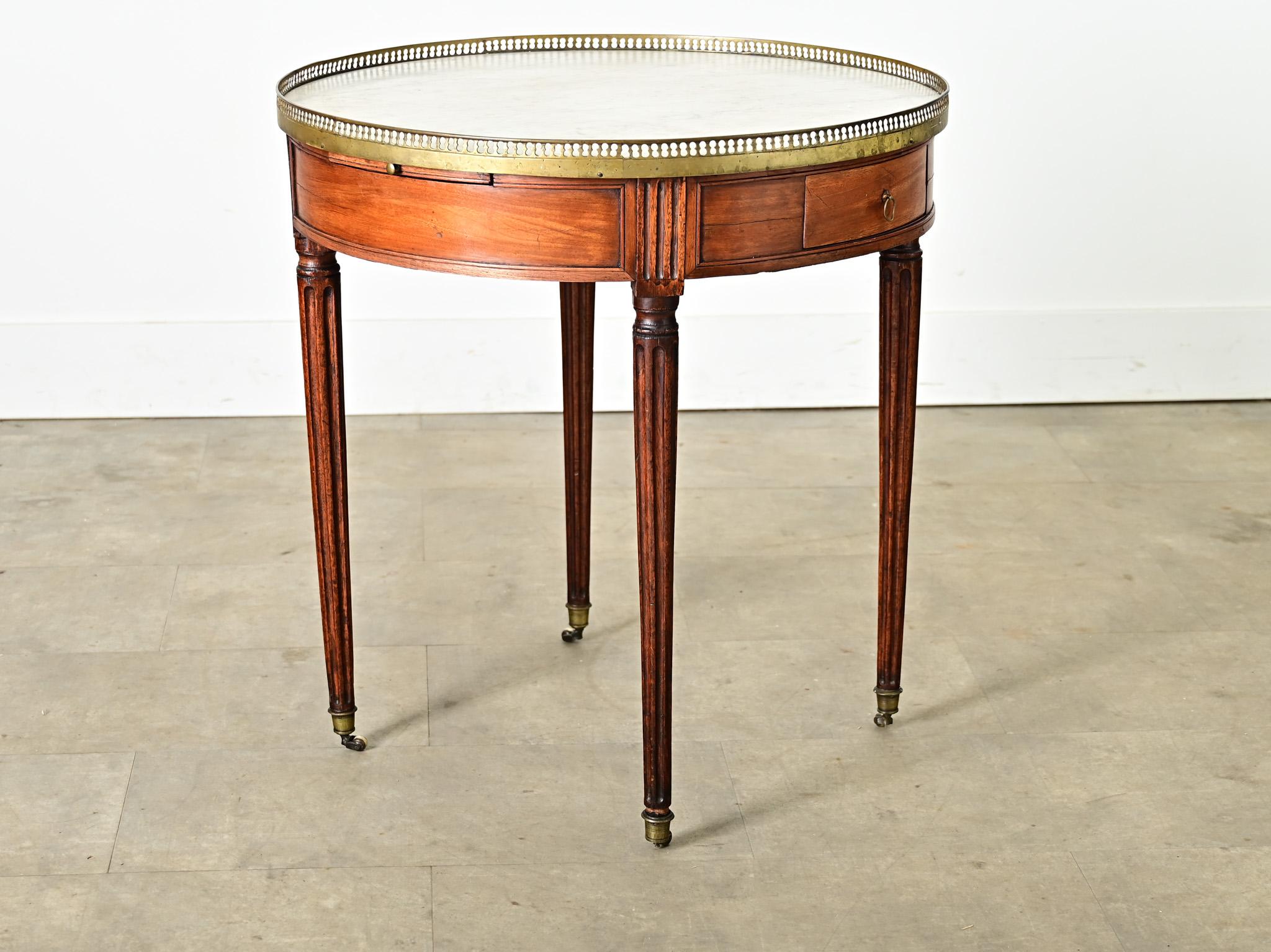 A French Louis XVI style mahogany gueridon-side table from the 19th century with a white marble top surrounded by a pierced brass gallery resting on fluted legs. This timeless table design is a classic example of form & function, made for the