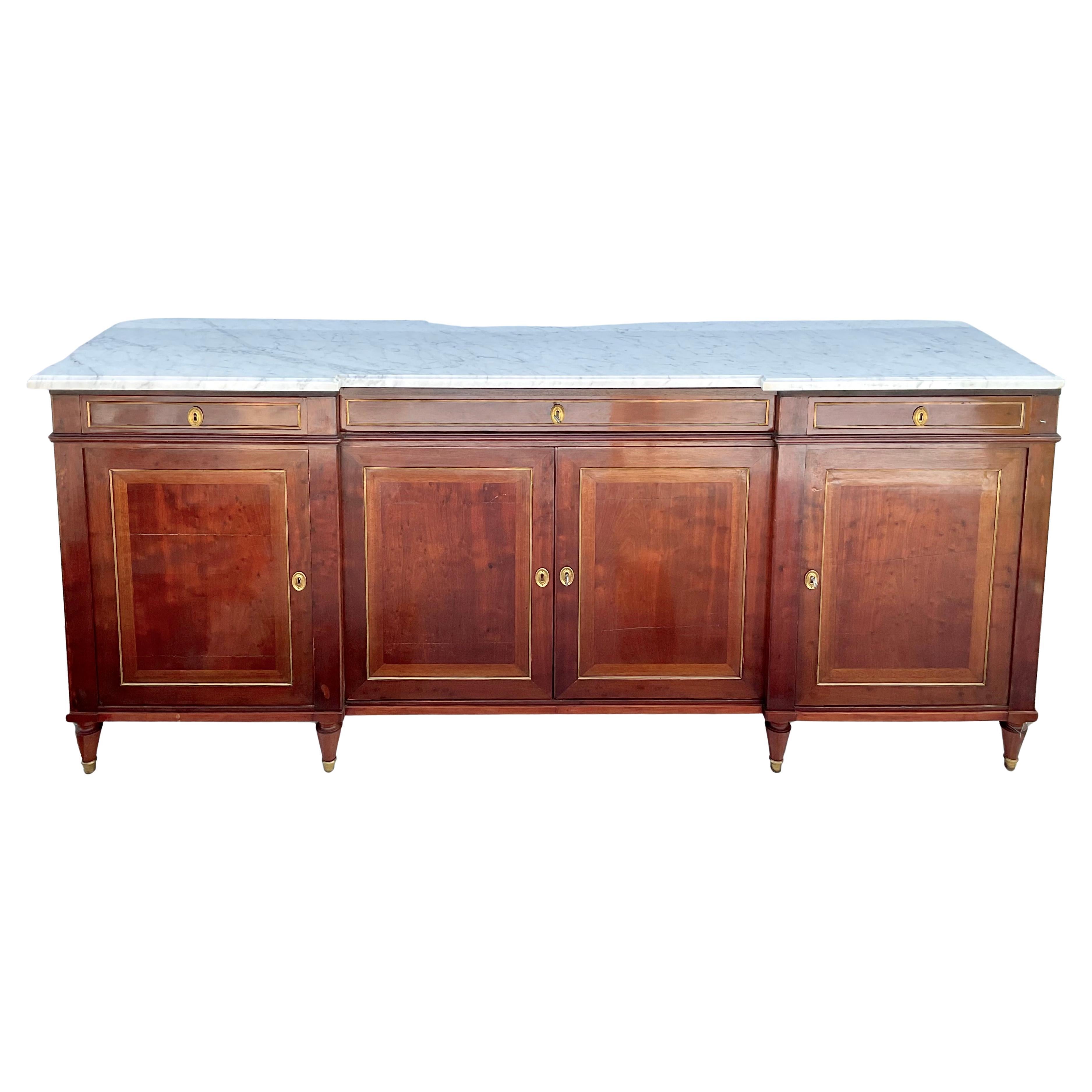 Monumental Louis XVI style walnut enfilade, having a Carrara marble top over three drawers and cabinets leading to interior shelf storage, featuring brass hardware rising on tapered legs ending in brass sabots. A truly stunning. impressive and