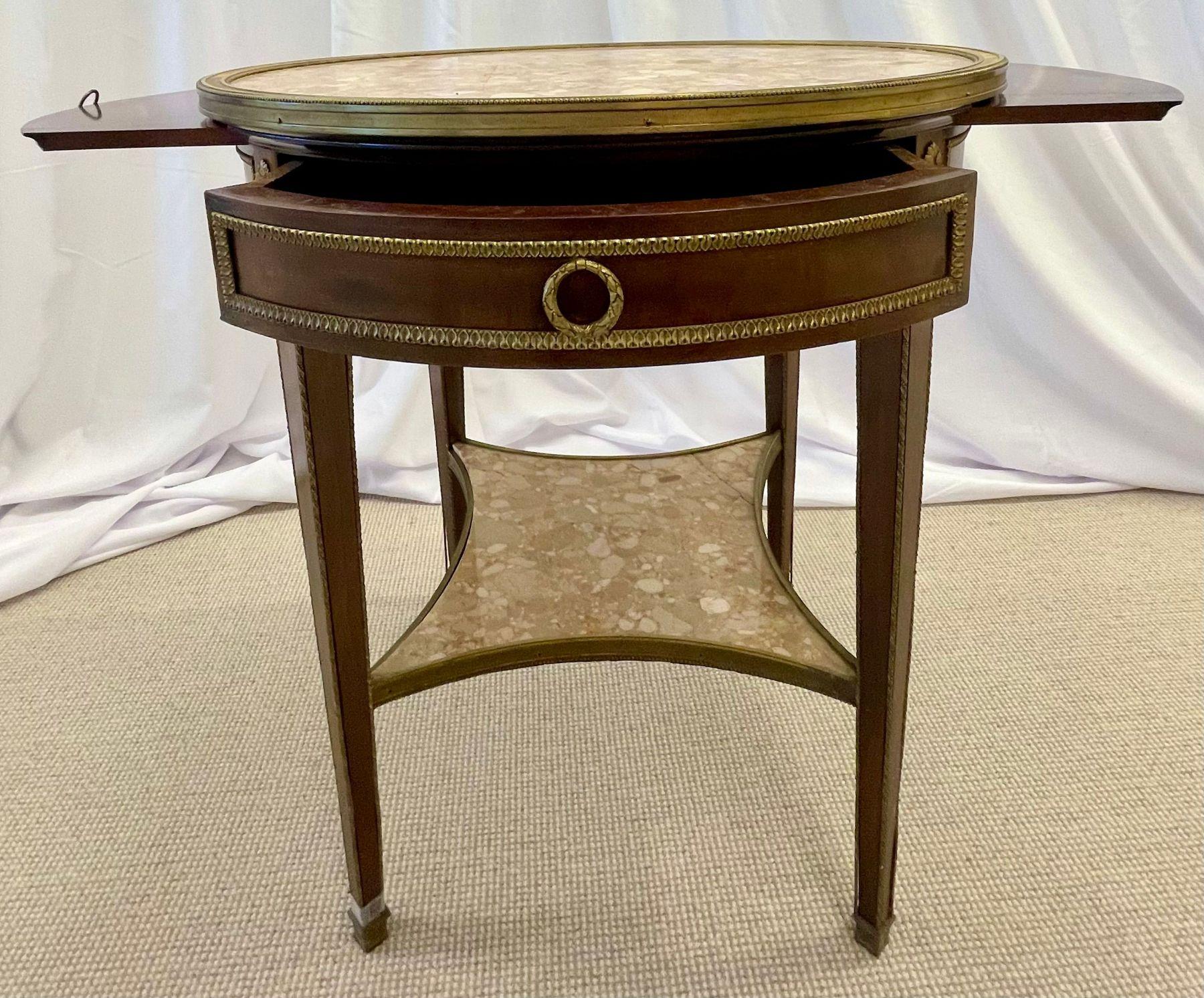 French Mahogany Louis XVI Style Marble Top Bouillotte Table, Bronze Mounted. A stunning example of the finest of bouillottes. This François Linke style end or side table sports the finest of bronze castings with a lower marble shelf used as an
