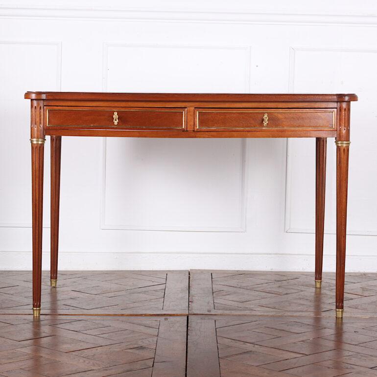 French mahogany Louis XVI style writing desk in mahogany with brass accents. Two drawers fitted to the apron and two false drawers on the reverse, the whole standing on fluted turned tapering legs with brass cuffs and feet. The piece has a