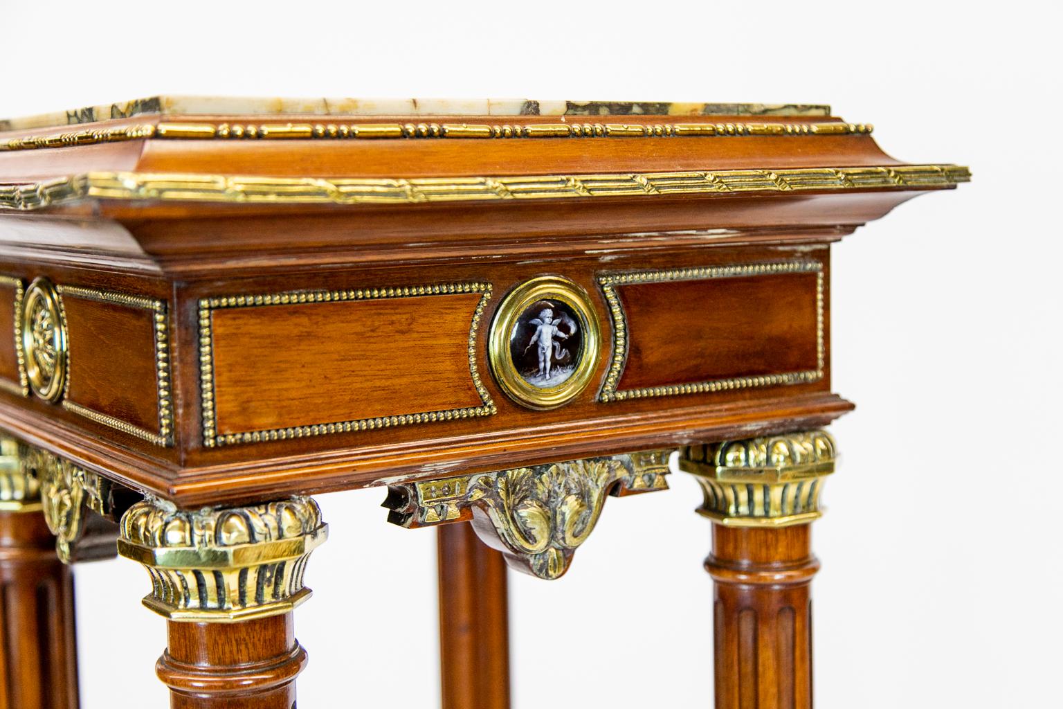 French mahogany marble-top pedestal on bun feet with heavy cast brass moldings and capitals, stop fluted columns and porcelain cartouche panels, one has a figure of a woman, and the opposite is a cupid with a torch.
 