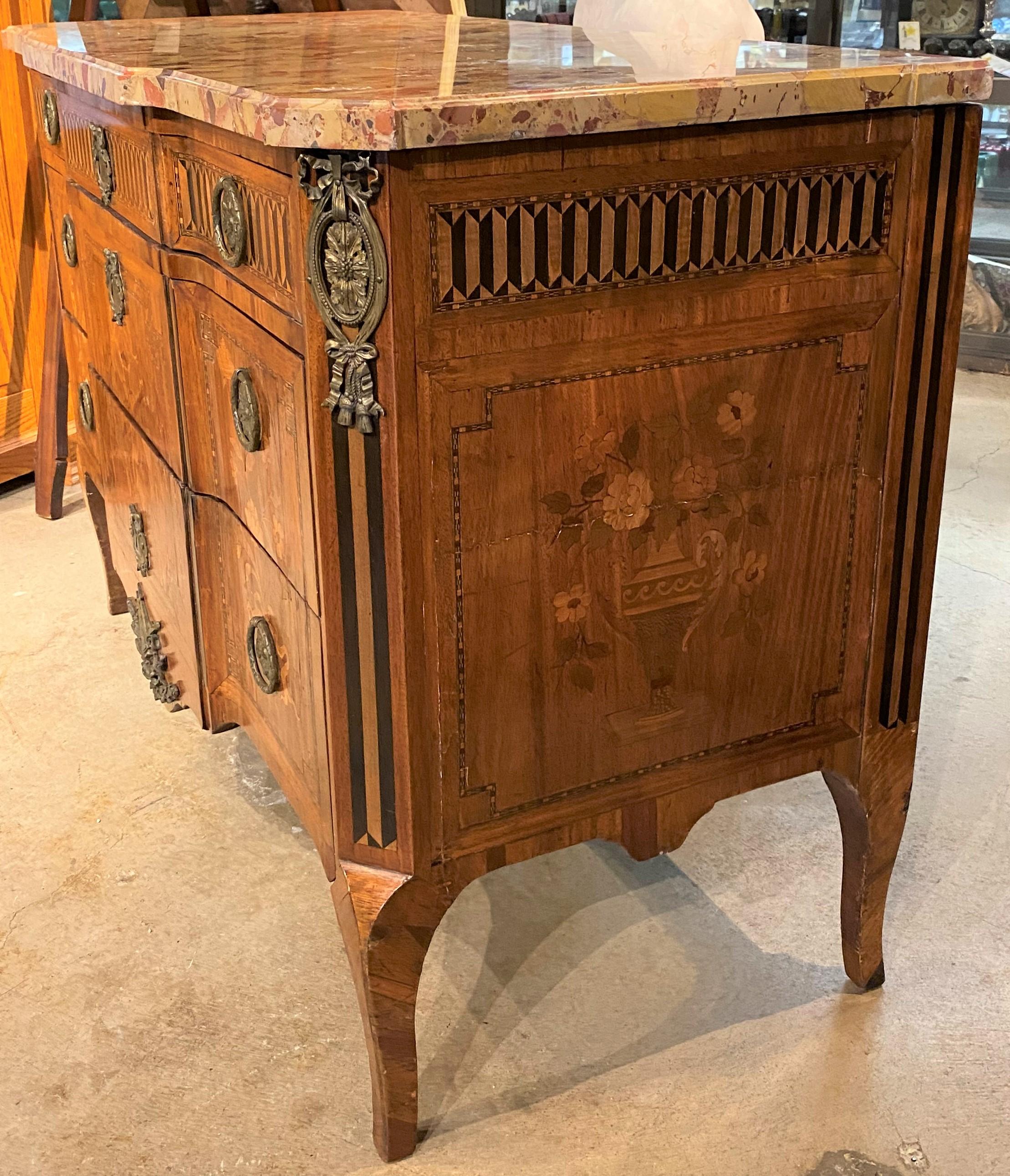 A beautiful French mahogany commode with fine marquetry, a conforming marble top with molded edges surmounting a case with three drawers, canted corners, applied ormolu on the corners, escutcheons, ring handles, and center drop, detailed foliate and