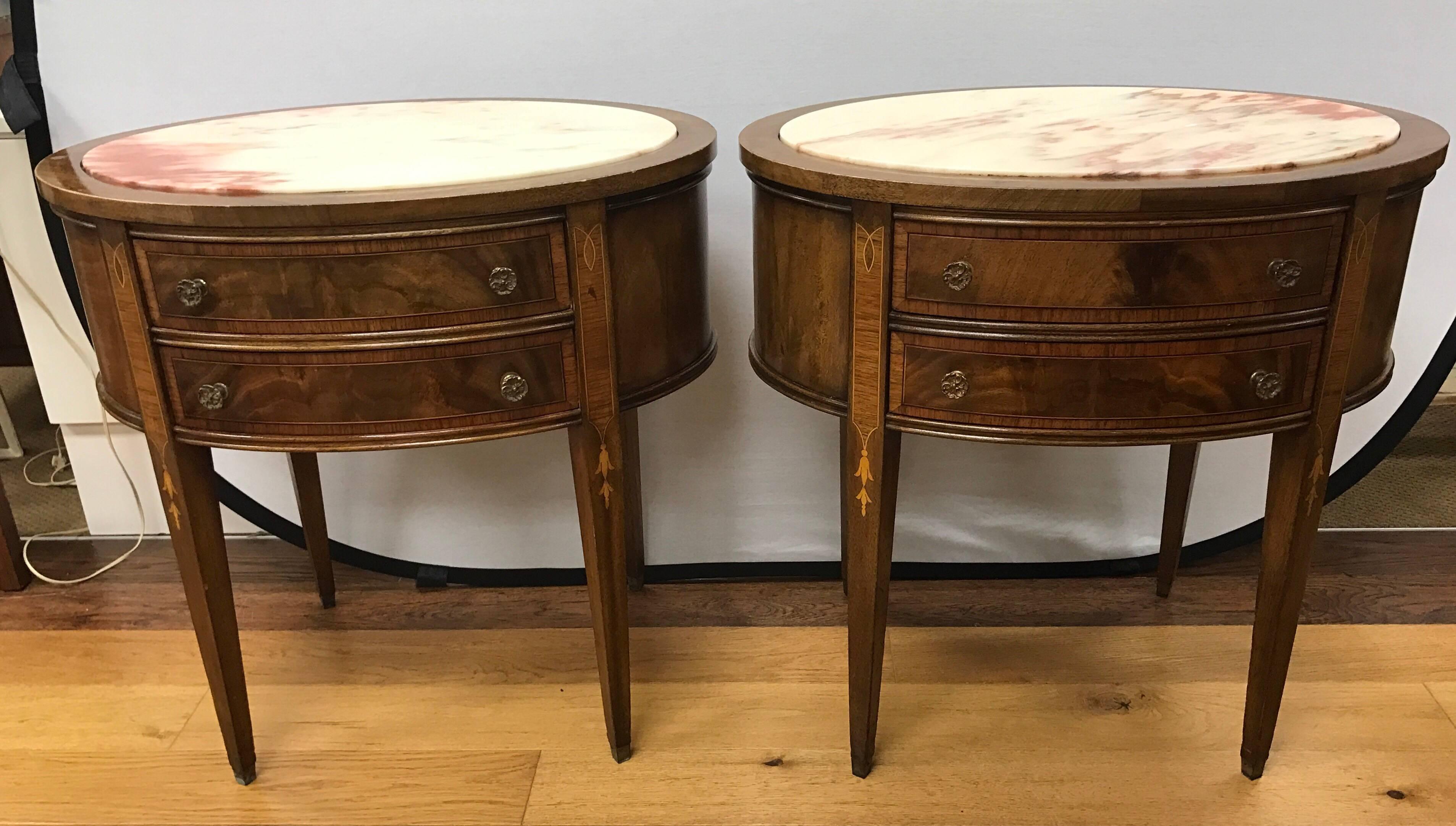 Pair of French mahogany two-drawer oval tables with inset marble tops and bell flower inlay.