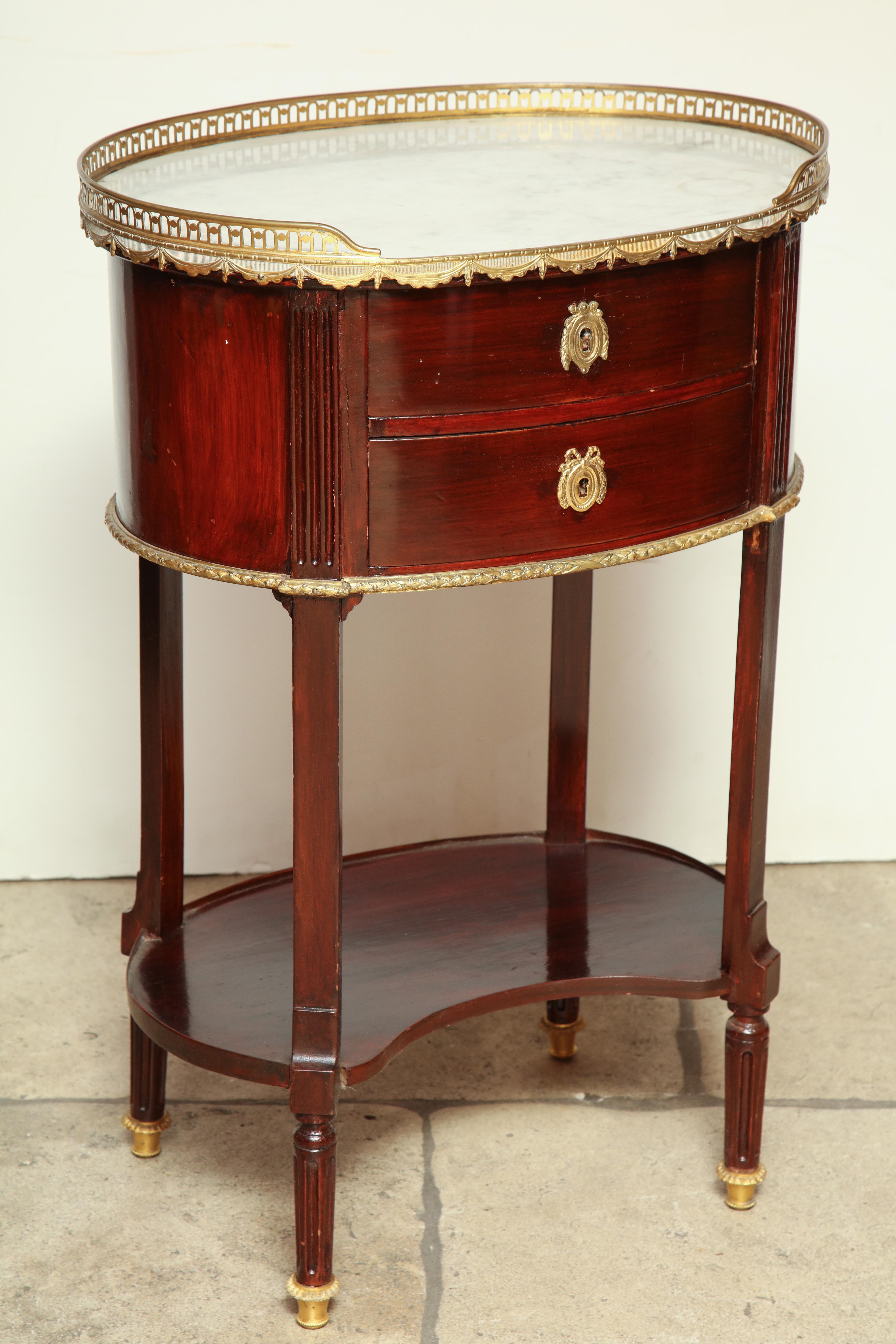French Directoire mahogany oval side table with a Carrara marble top, bronze drapery pierced gallery trim, two front facing drawers, fluted legs and a kidney form shelf stretcher base.