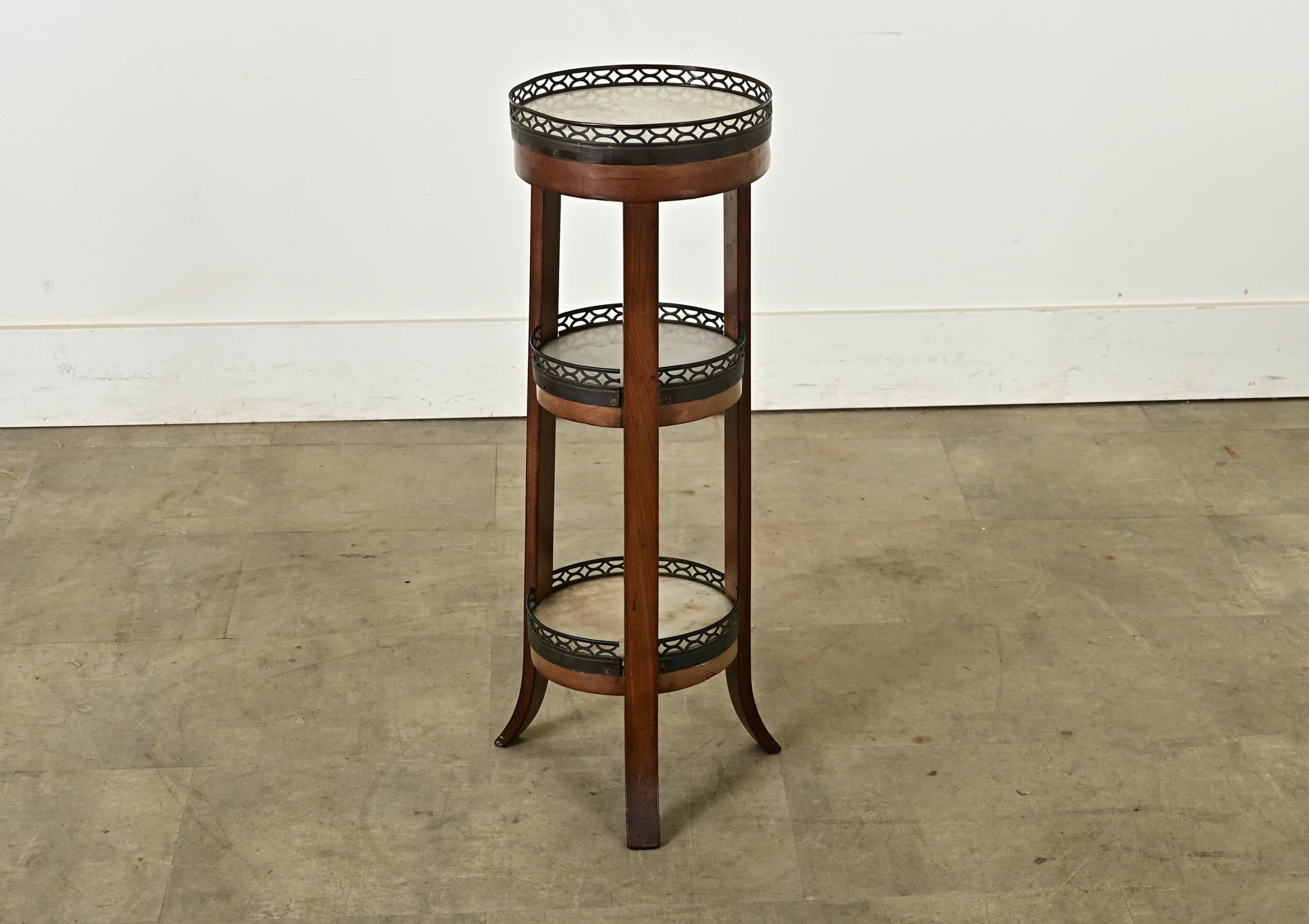 A small-scale gueridon table from France, 19th century, offering three display shelves. Each tier is crowned with a pierced brass gallery mounted to the wood frame holding an inset marble disc for displaying small treasures or resting one’s