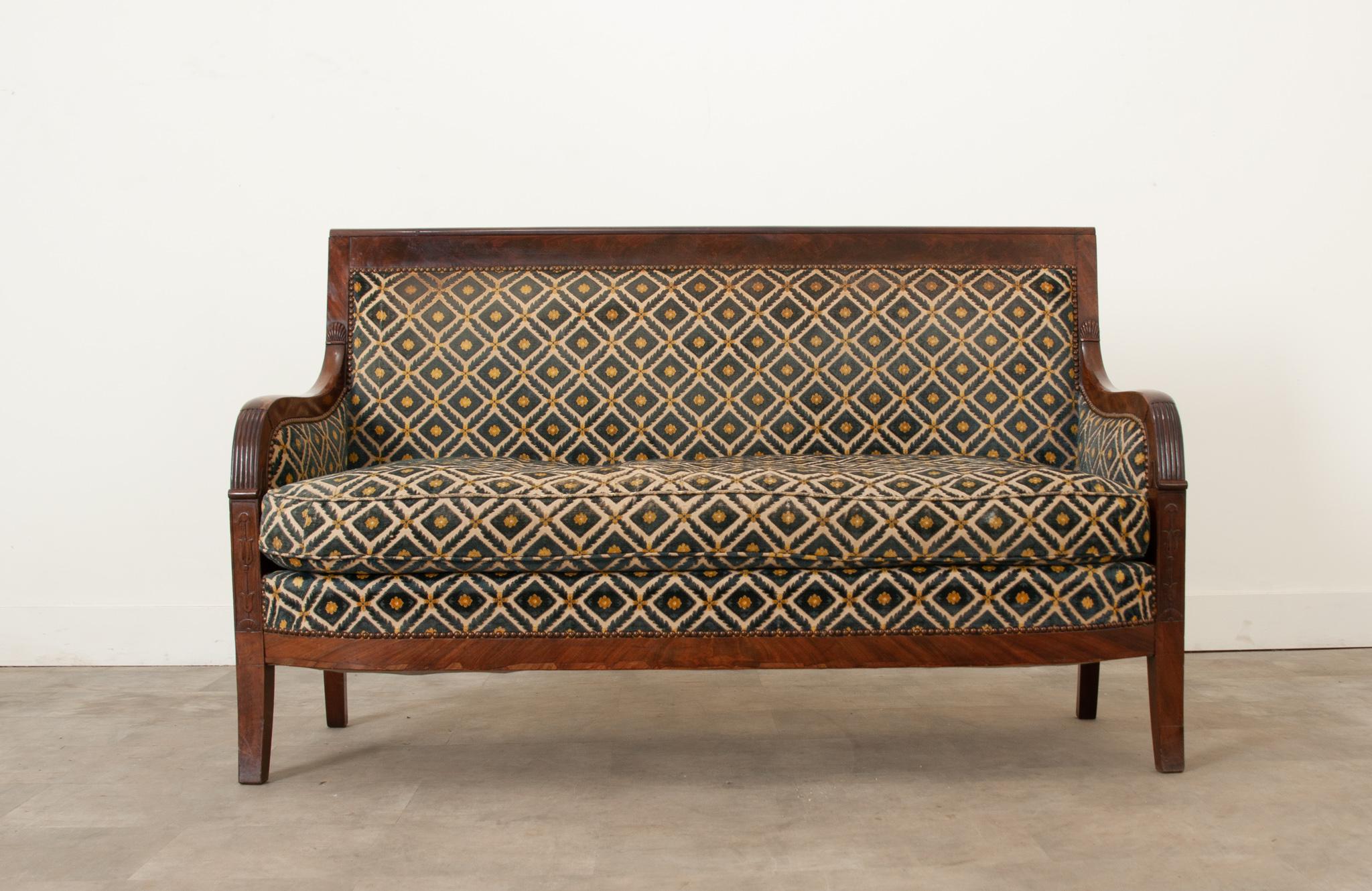 A classic French Restauration mahogany settee. This 19th century piece is made out of solid mahogany and a comfortable, intricately patterned cushion. The fabric is a worn cut velvet upholstery with a nailhead trim.
 The seat height is 19”H , arms