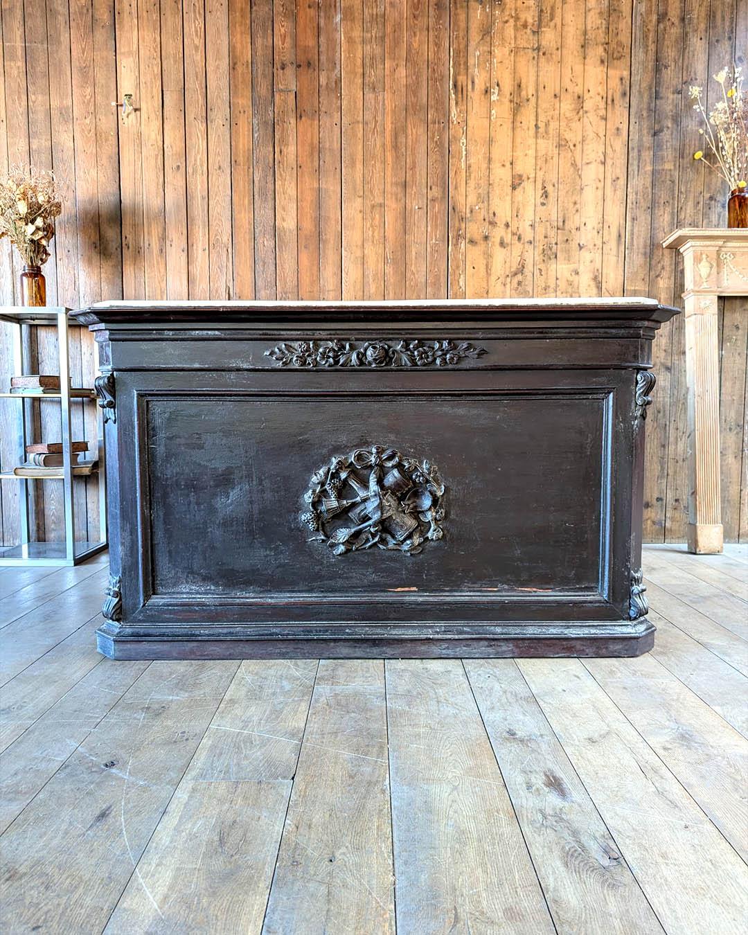Elegant 19th-century French store counter in solid mahogany with its original marble top. This richly carved piece features detailed floral motifs and a central medallion adorned with symbols of abundance, including grapes and pomegranates. The