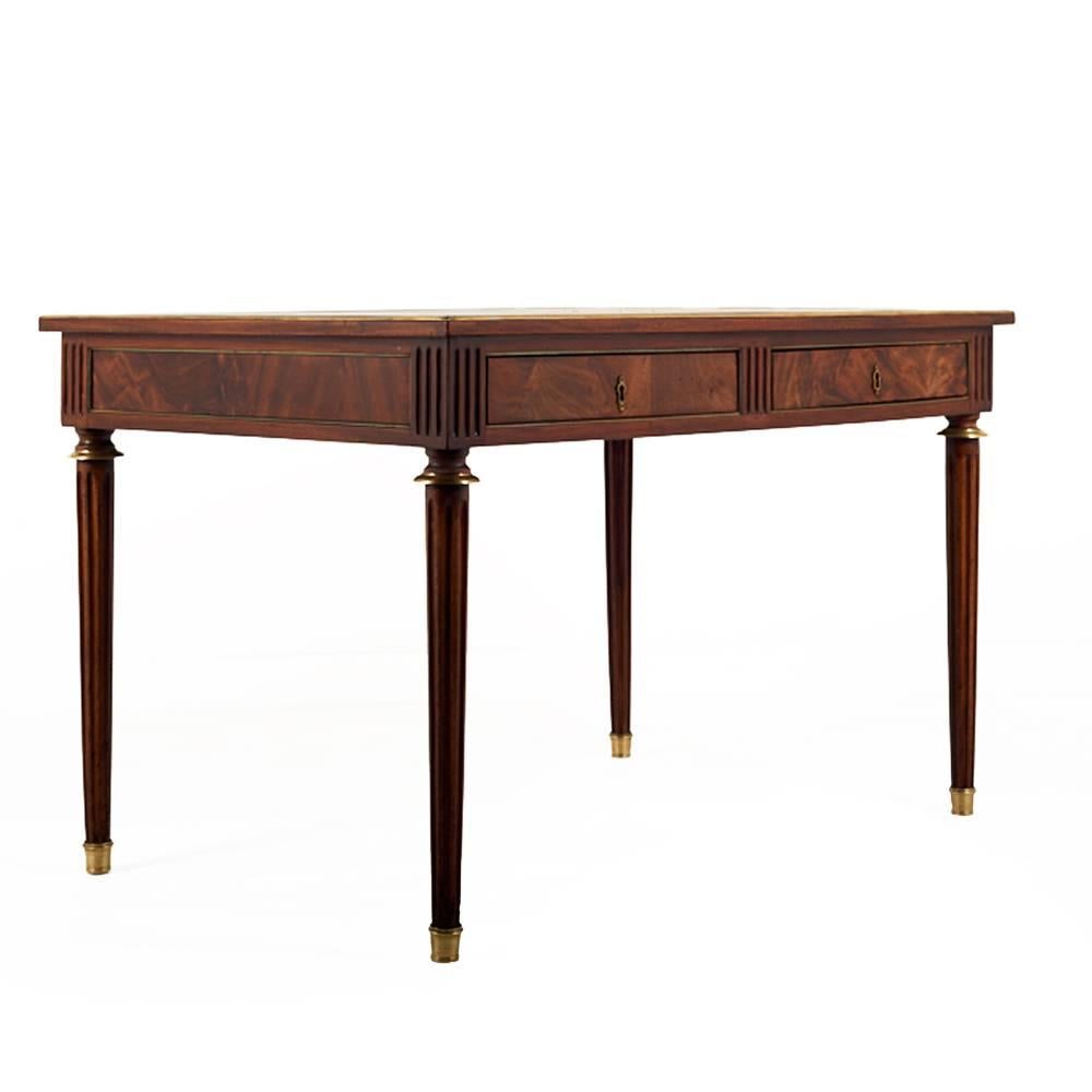 A French flame mahogany Napoleon III writing table with two drawers and a gilt tooled cognac color leather top.

The desk is finished on all four sides in flame mahogany and brass trim and is raised on tapering fluted legs with brass feet and