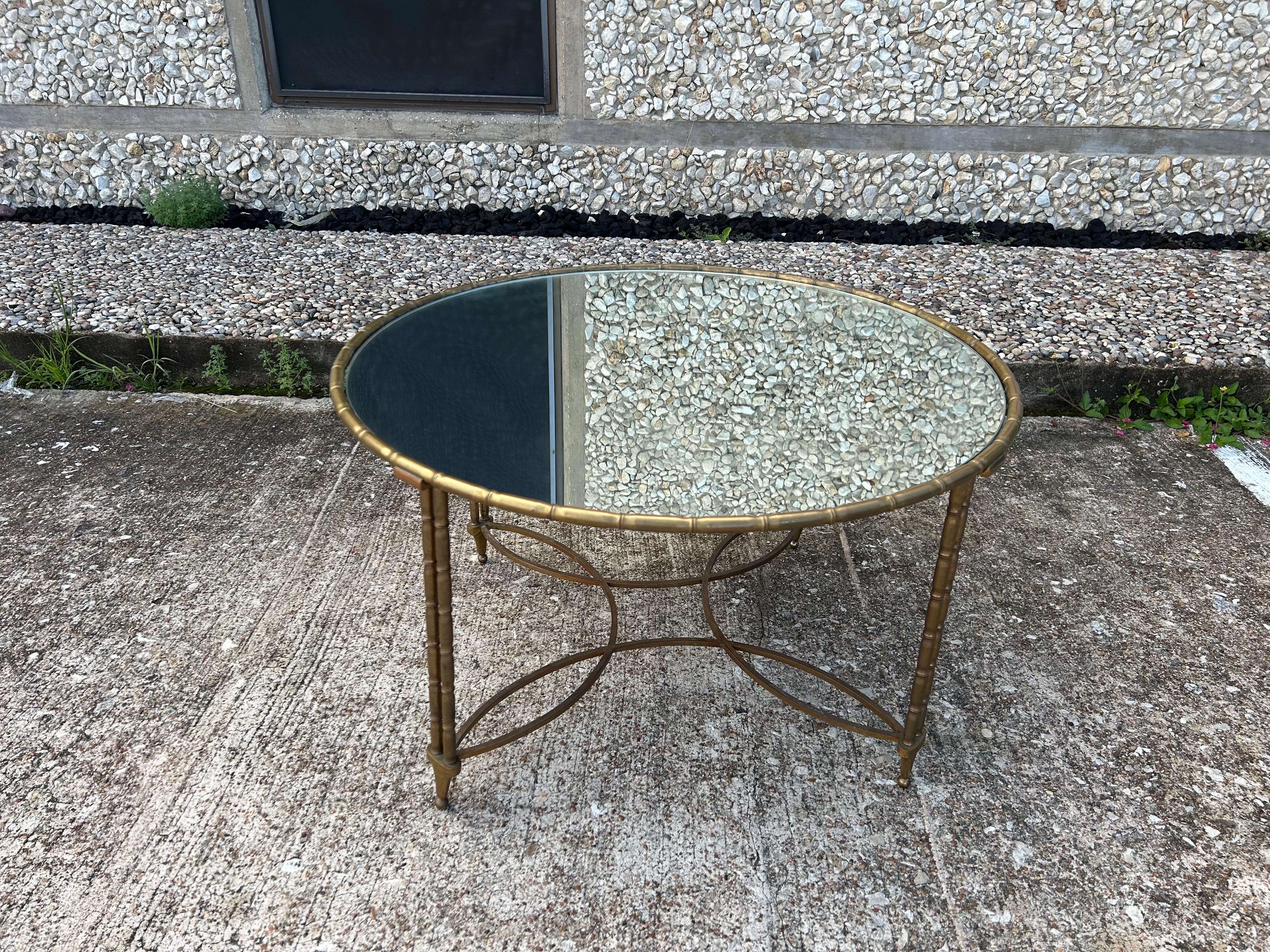 French Maison Baguès Style Brass Coffee Table.
Offered is a French Louis XVI style round faux bamboo brass coffee table with beautiful cross bands connecting legs and a mirrored top. This chic French modern cocktail table is versatile enough to be