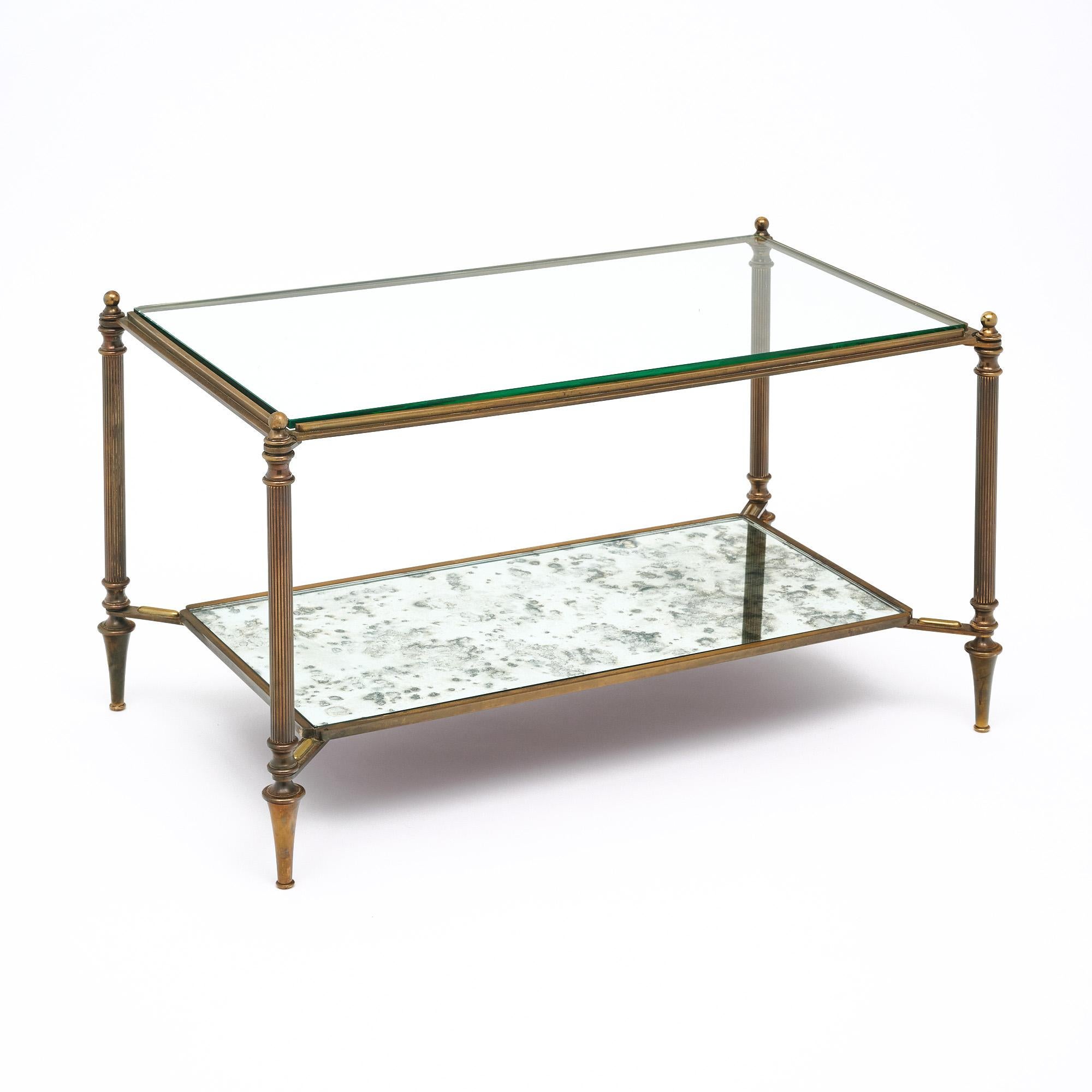 French Maison Baguès coffee table made of gilt brass. We love the finely cast details throughout. This piece has a clear glass top and an antiqued mirrored lower shelf. 
