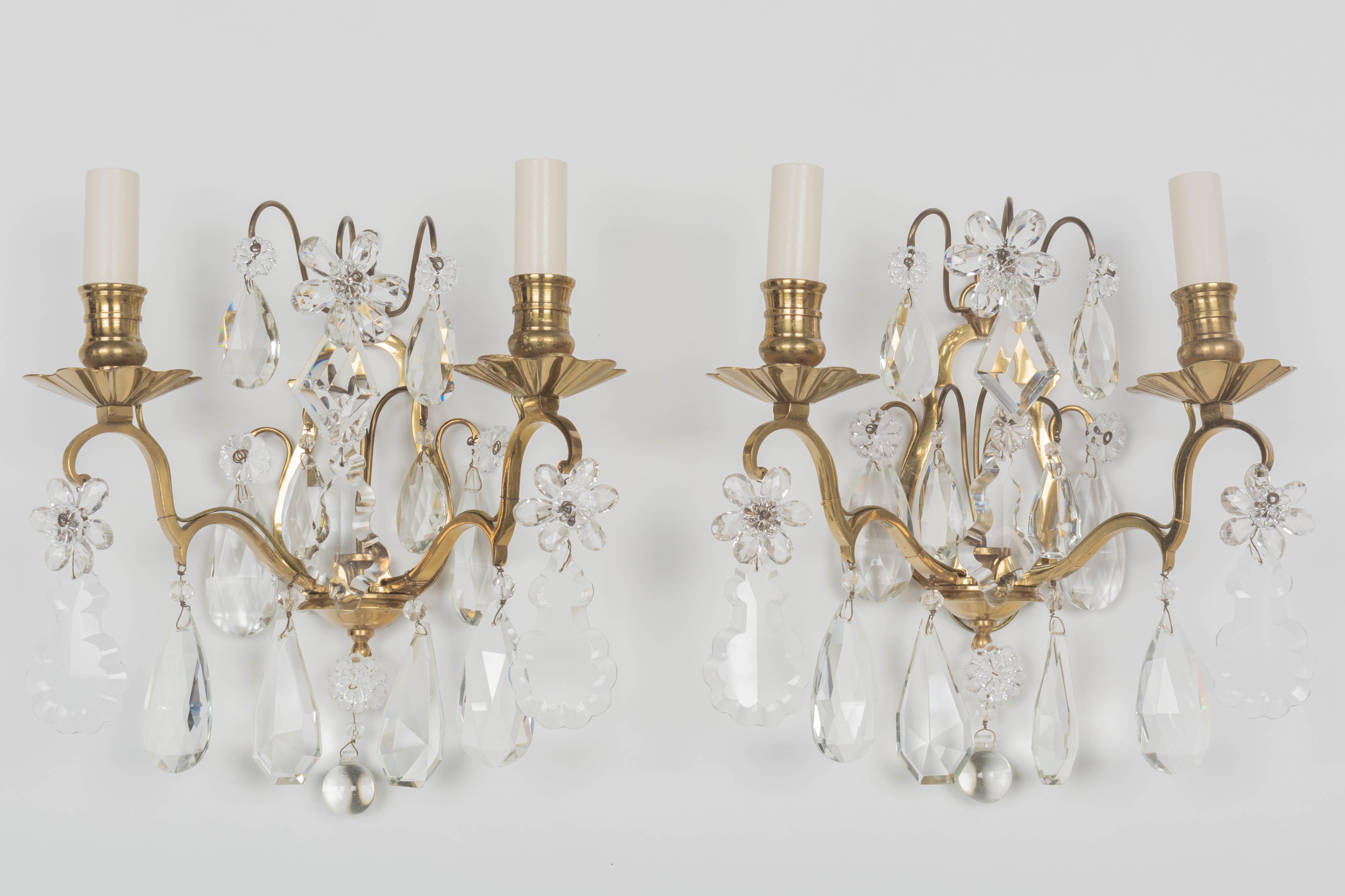 A pair of French Maison Baguès cast brass and crystal sconces. Good quality heavy casting with two scrolled candle arms and a variety of cut crystal teardrop pendalogues and faceted crystal flowers with rosettes. All original prisms. Rewired with
