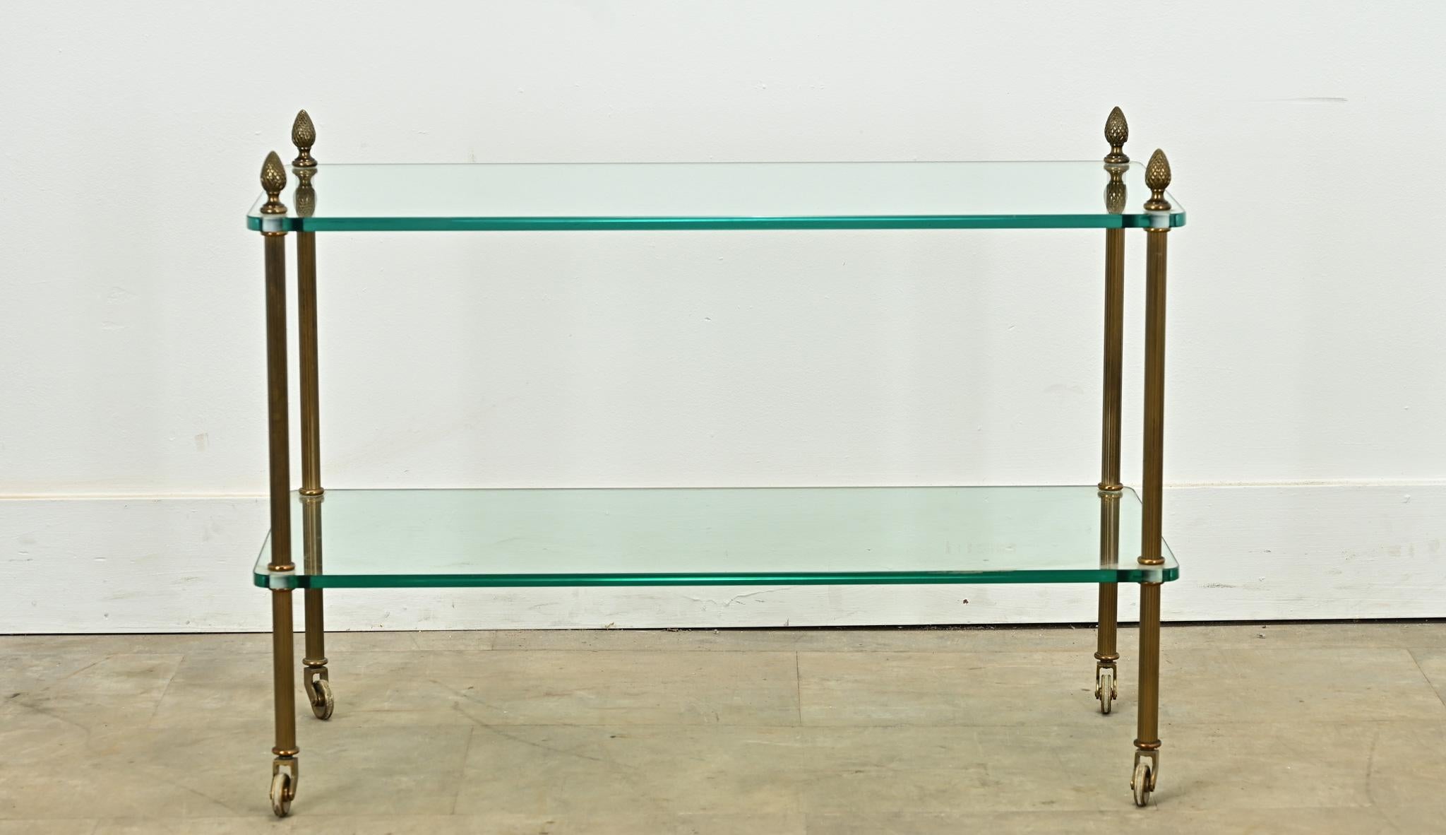 Table d'appoint en gradins du milieu du siècle dernier, fabriquée par la Maison Charles. Cette table est composée de deux niveaux de verre aux angles arrondis. Quatre pieds-colonnes cannelés en laiton, surmontés de fleurons décoratifs, relient les