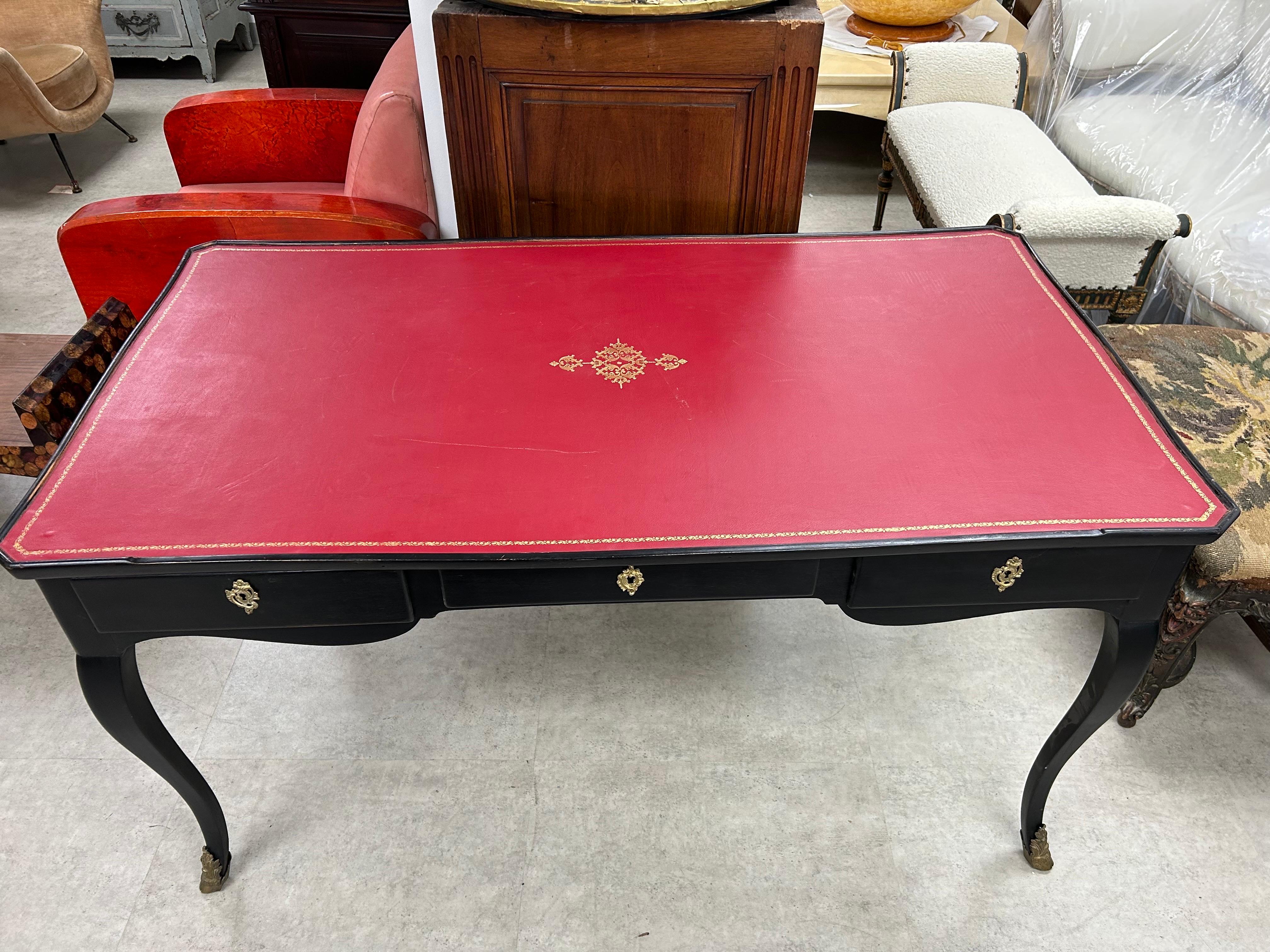  French Maison Jansen Attributed Louis XVI Style Ebonized Desk.
We offer a gorgeous antique French Louis XVI style ebonized desk or bureau plat with a red leather top embossed with gilt, three drawers and beautiful bronze sabots.
This desk has the