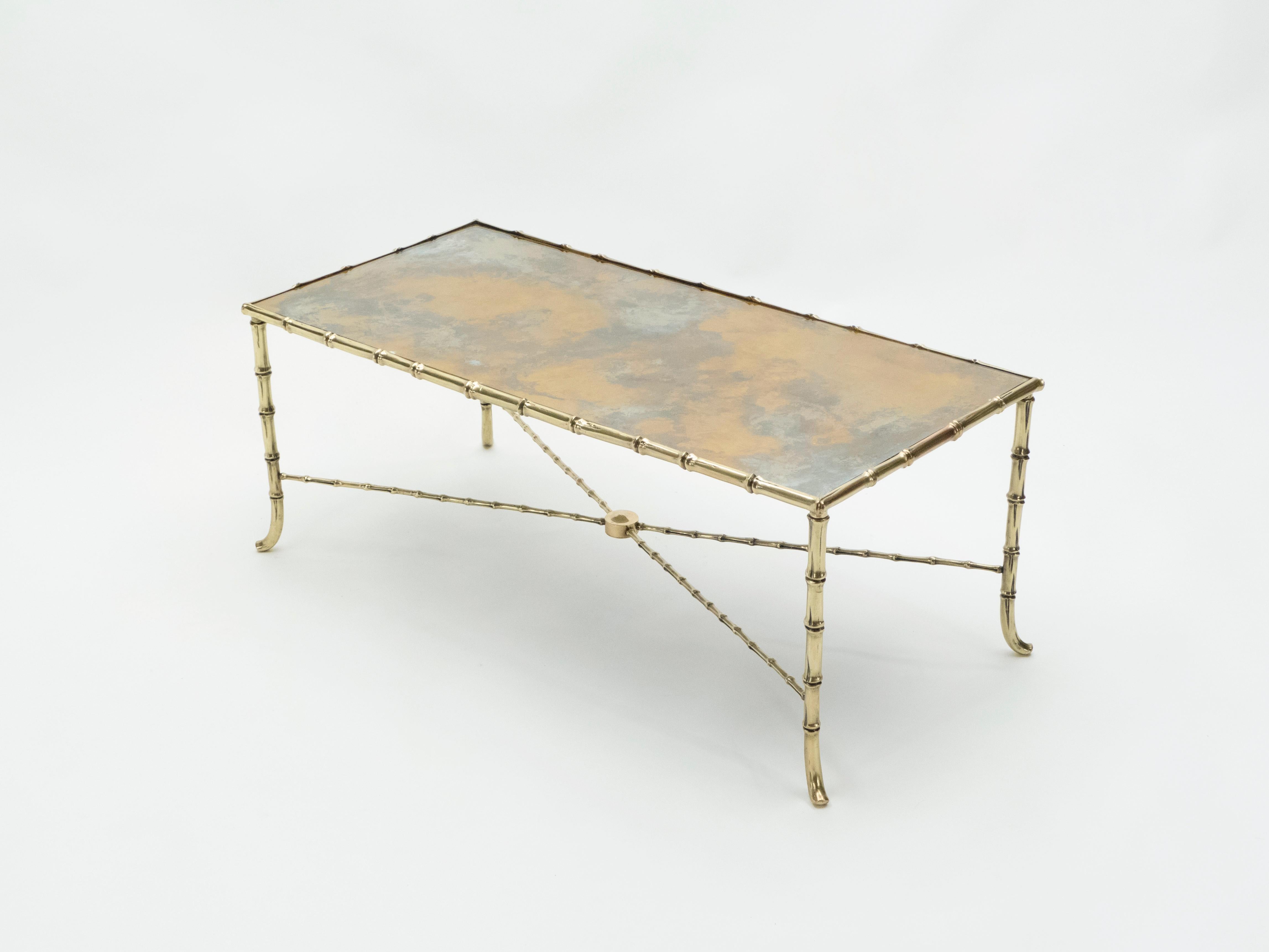 This coffee table by French design house Maison Jansen was created with solid brass and typical French neoclassical brass bamboo and old patina mirror, circa 1960. The old patina mirrored top is smooth, while the brass bamboo feet provide an
