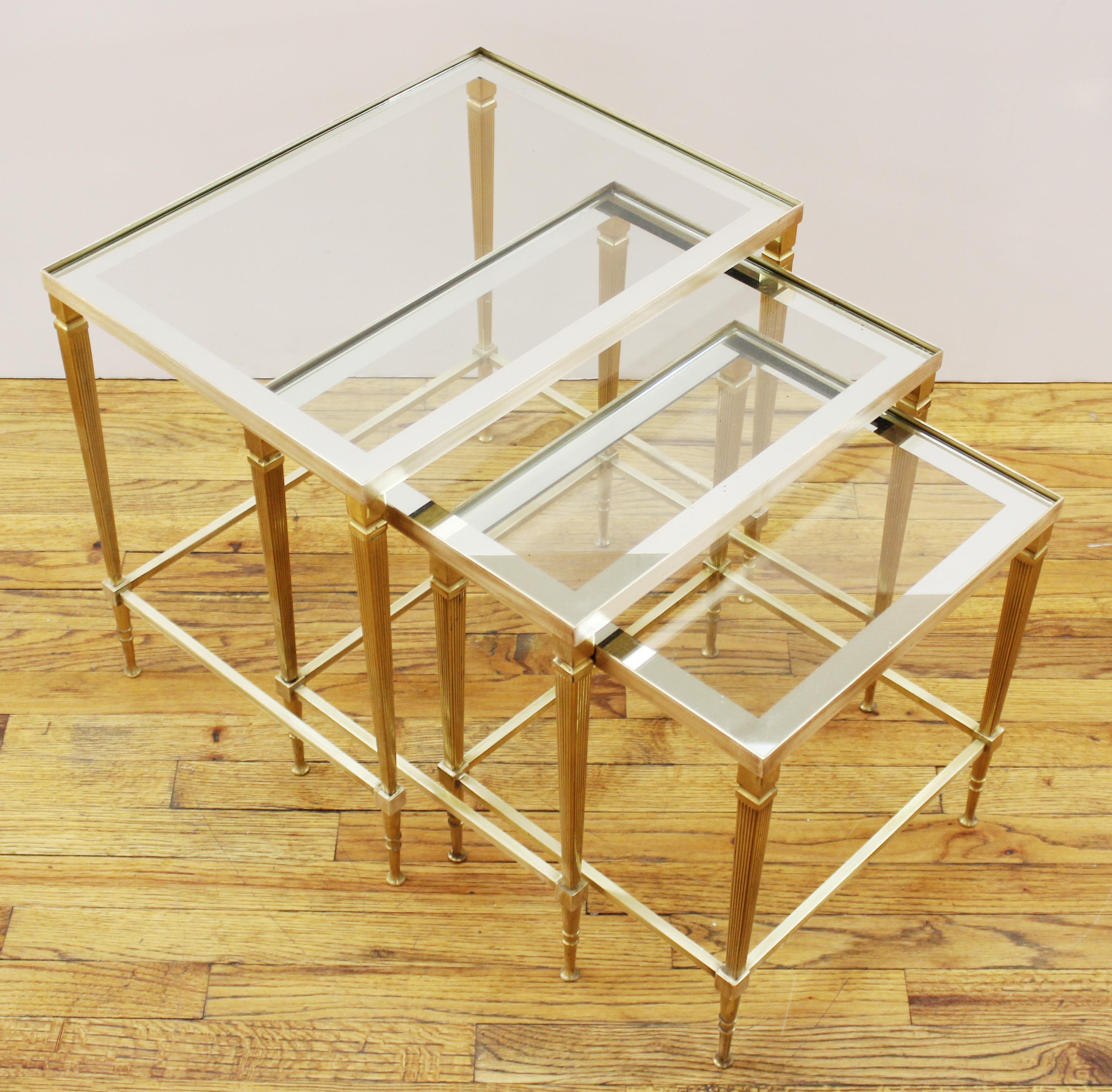 Nest of three midcentury French Maison Jansen style brass occasional or end tables with glass tops banded with a mirrored border. Measures: 18.5
