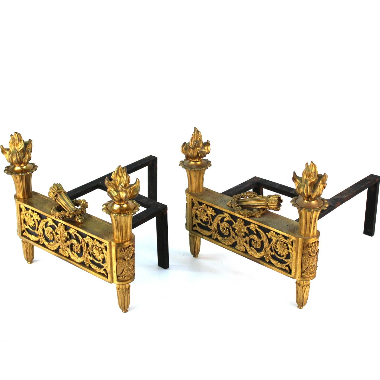 A pair of Maison Jansen style andirons in French Directoire style, made of gilded bronze. Intricate 18th century style decorative motives and torches adorn this impressive pair of fireplace accessories. Great condition, with original patina. No
