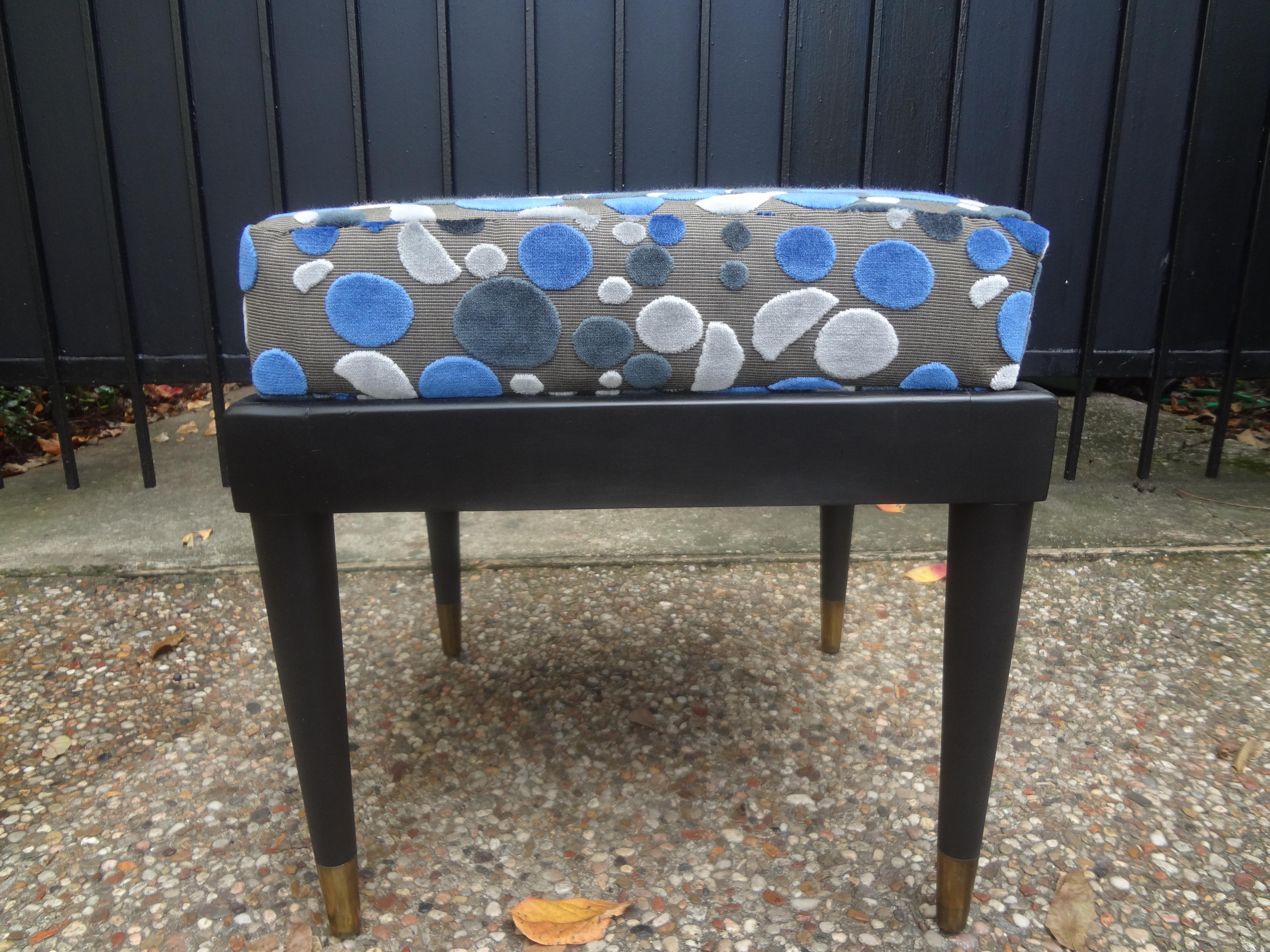 French ebonized ottoman in the manner of Maison Jansen. This stunning French ottoman, bench or stool has a matte Ebonized finish, tapered legs with brass sabots. This French Mid-Century Modern bench has been newly upholstered in a beautiful cut