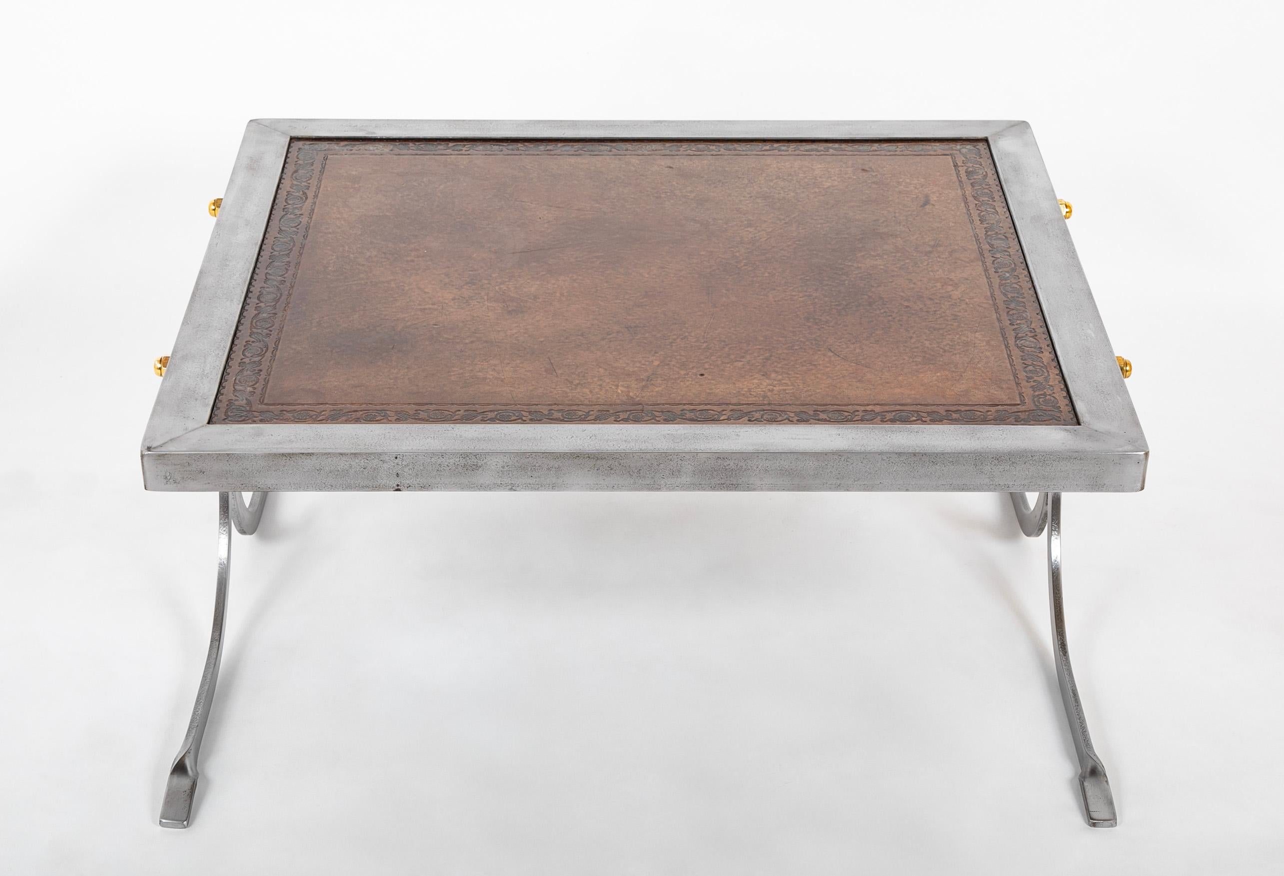 Dieser Tisch ist eine gelungene Verbindung von Moderne und Tradition: ein stromlinienförmiger Eisensockel, der mit Messingmuttern zusammengehalten wird, und eine klassische Lederplatte mit dekorativem Rand. Das schlichte Profil, eine Hommage an Jean