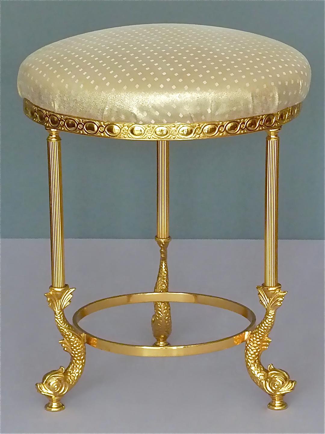 Fantastic and rare high quality gilt bronze brass metal three-leg dolphin vanity stool or side chair by Maison Lancel, France around 1950s to 1960s. The neoclassical midcentury dolphin stool with golden shimmering fabric upholstery in Hollywood