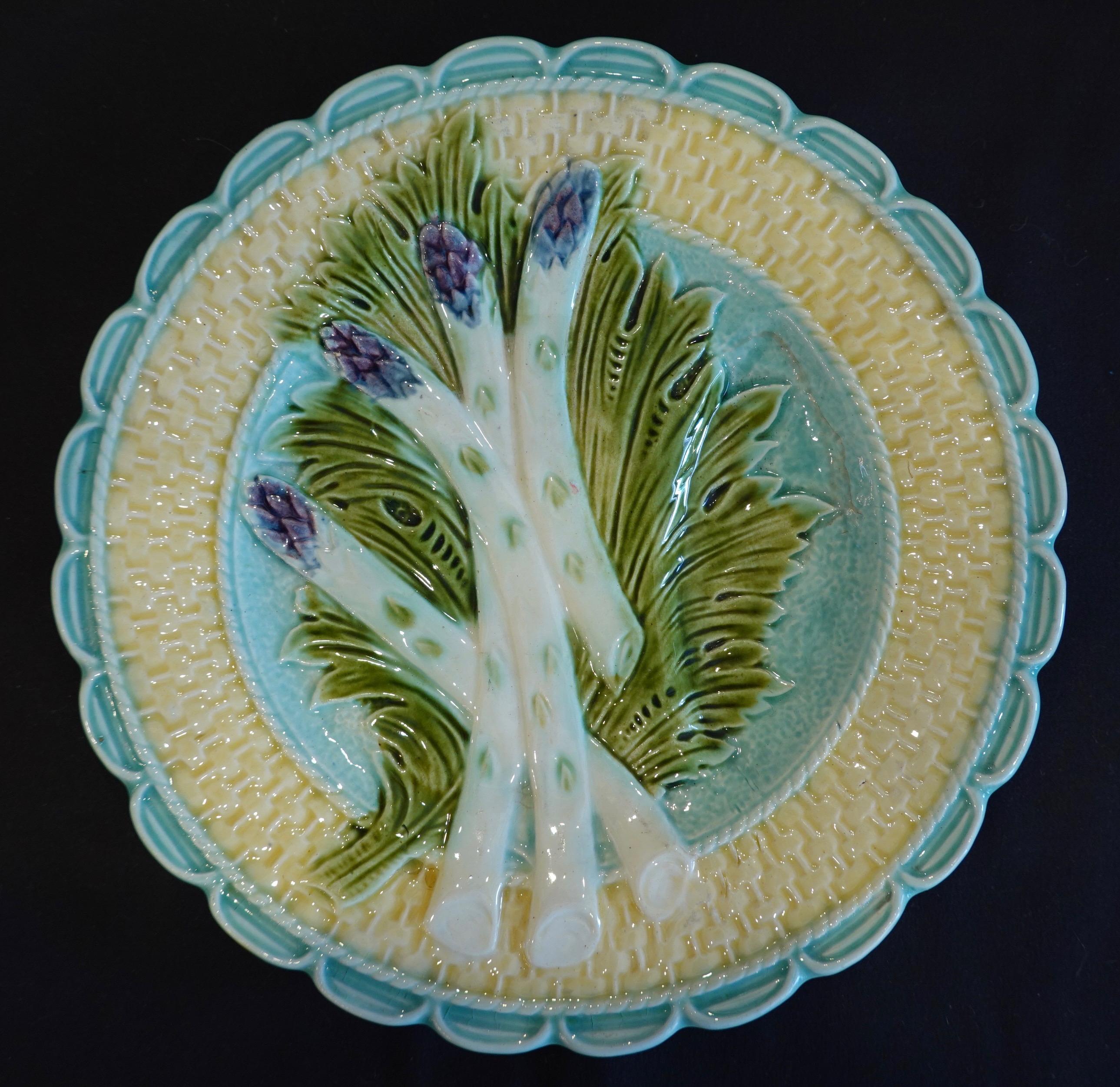 A colorful and highly-decorative Majolica asparagus plate featuring four asparagus spears resting on a leaf on a turquoise ground with tan basket weave around the edge. The plate is unmarked but clearly attributed to Salins.

The earthenware
