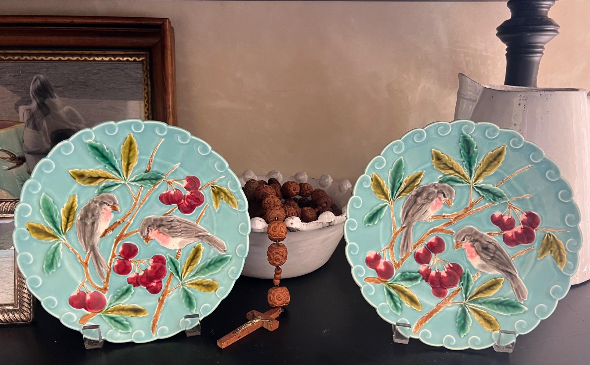 Ensemble de 2 assiettes anciennes en majolique, fabriquées vers 1900 en France. Les assiettes sont ornées d'un oiseau et de cerises sur le devant et d'un motif de volutes sur le pourtour.  Chacun d'entre eux est estampillé sur le fond.

