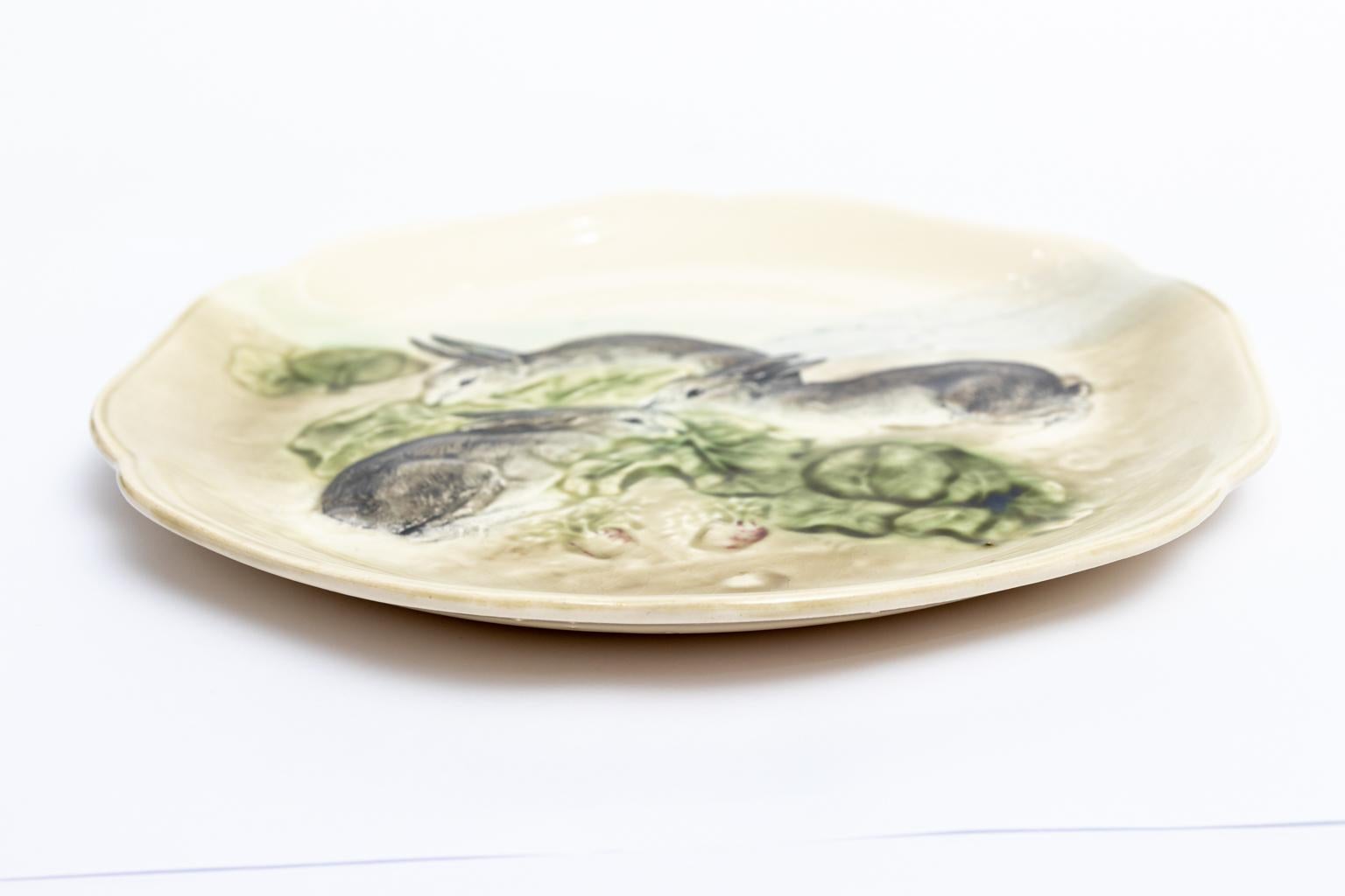 Circa 1900-1909 Majolica pottery bunny themed plate with scalloped trim produced in France in the early 1900s by New York based glassmaker Higgins & Seiter Company. The plate features three painted bunnies eating green lettuce leaves. Please note of