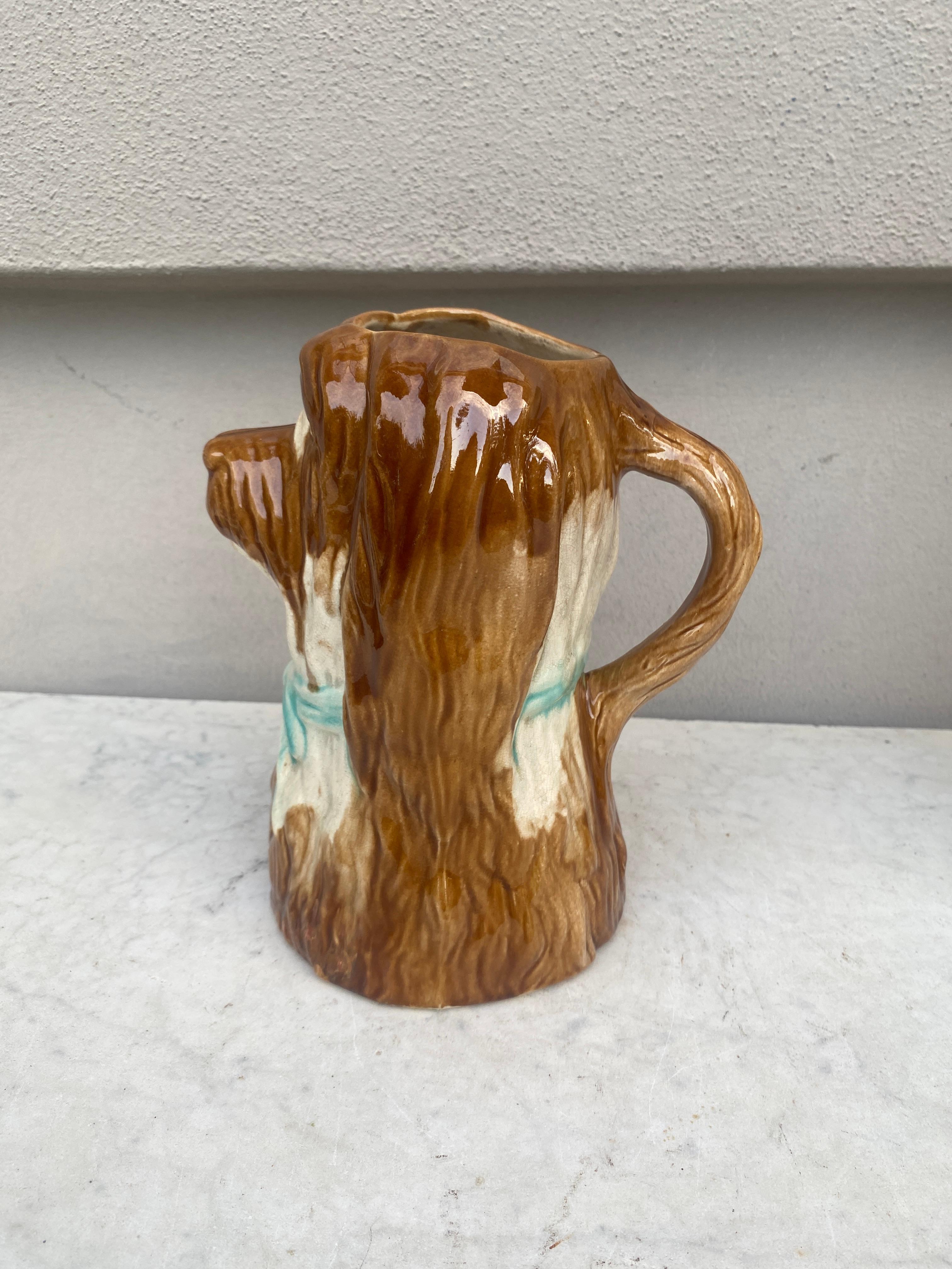 Pichet à chien en majolique française, vers 1900.
Chien blanc et marron avec un nœud bleu.