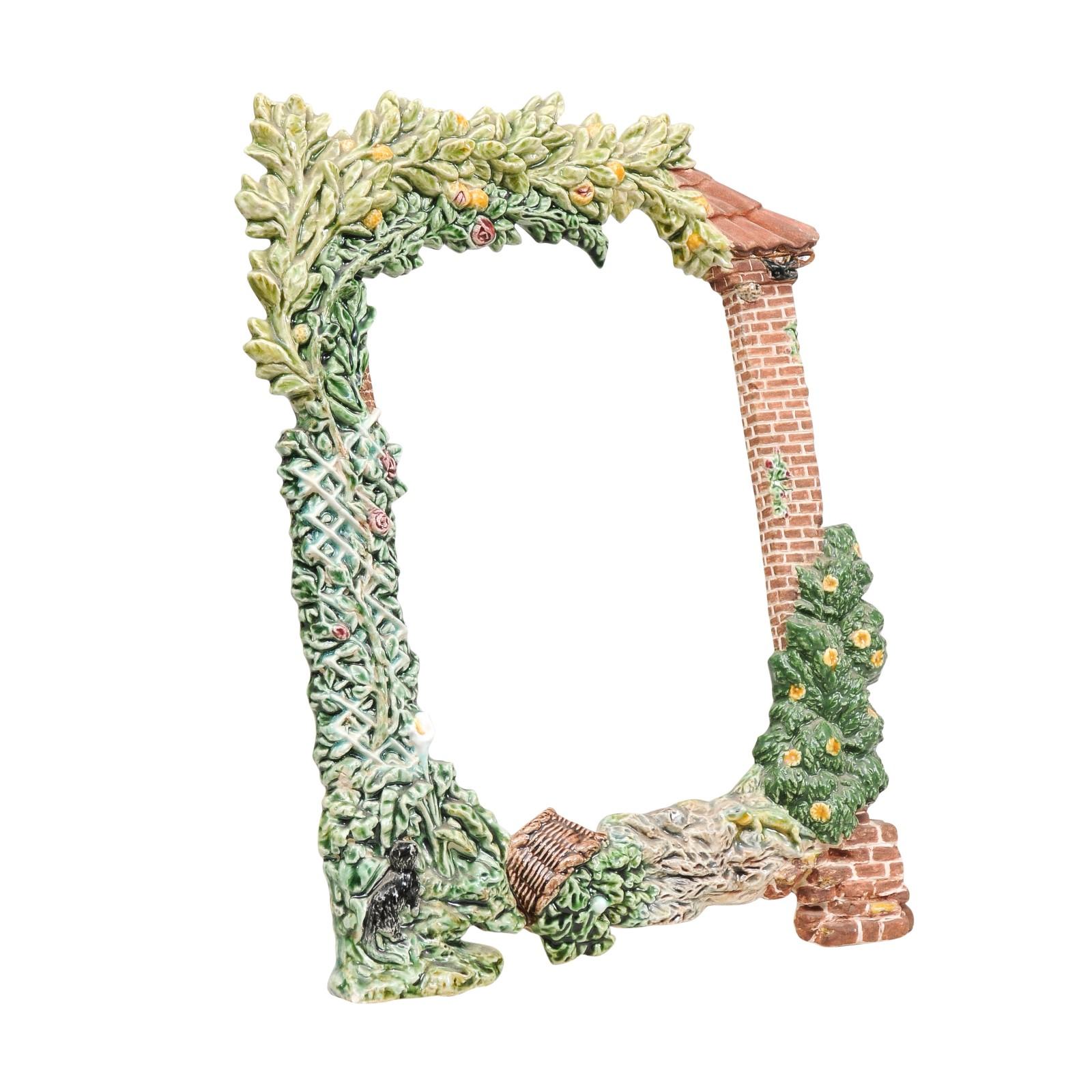 A French majolica frame from the 20th century depicting the side of a façade covered with foliage and trellis. Created in France, this majolica frame charms us with its lively depiction of the portion of a red brick façade supporting a red tiled