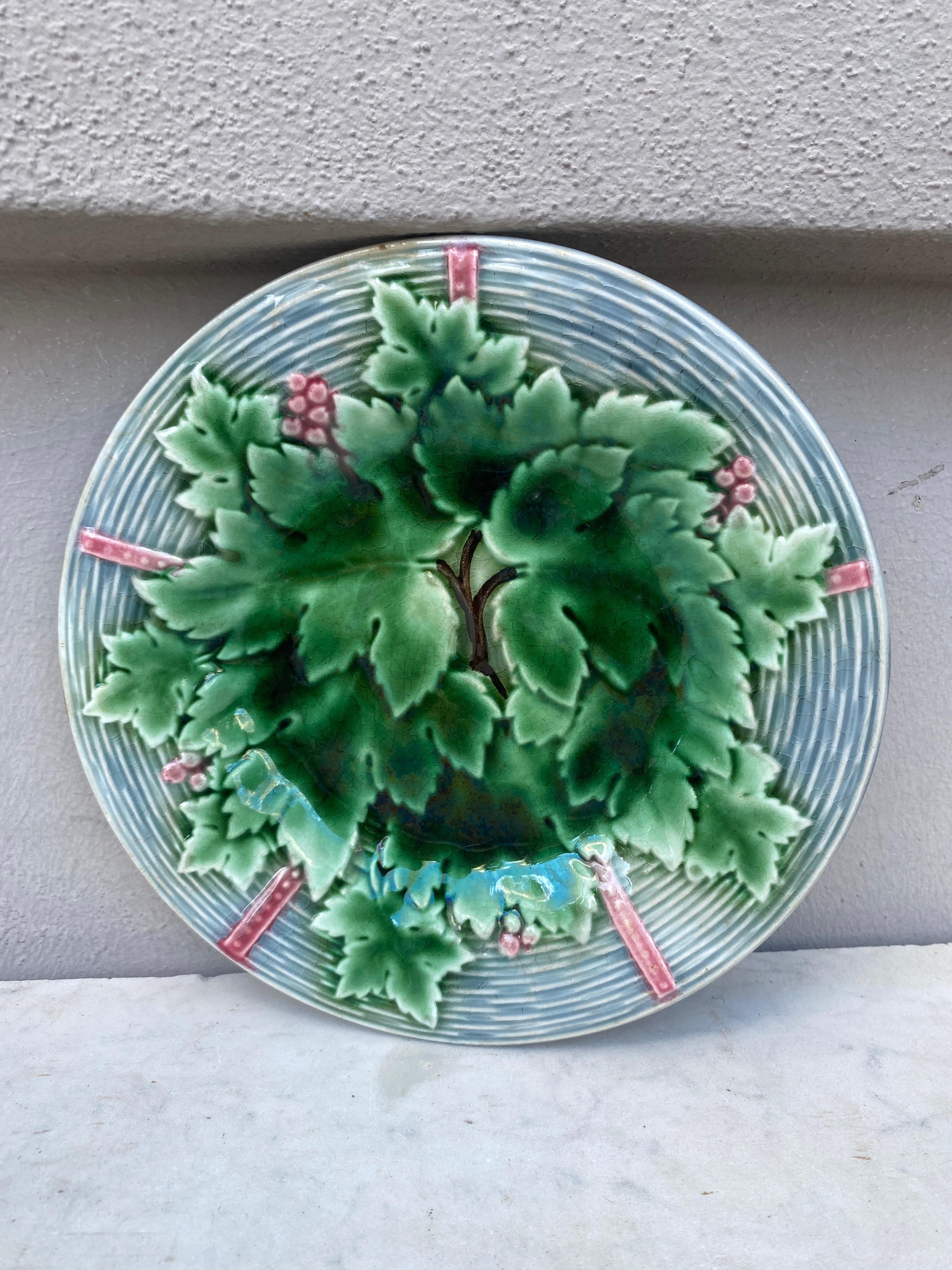 Grazioso piatto in maiolica francese con uva e foglie su uno sfondo grigio a trama di cesto firmato Gien, circa 1890.
