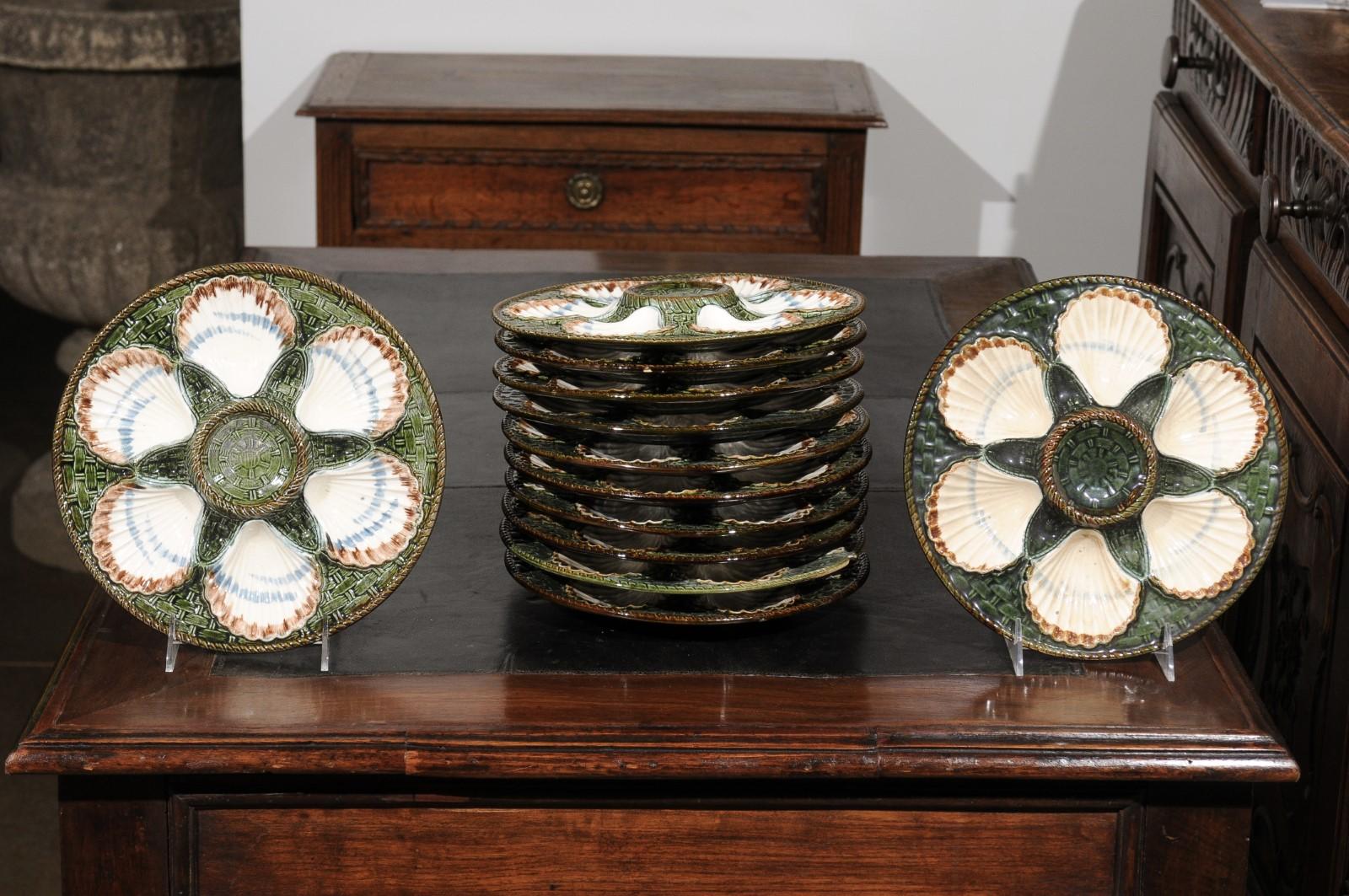 A French majolica Longchamp Terre de Fer scallop plate from the 19th century with green and brown accents. We have 6 plates available, priced and sold individually. Born in France during the 19th century, this scallop plate presents a green, white