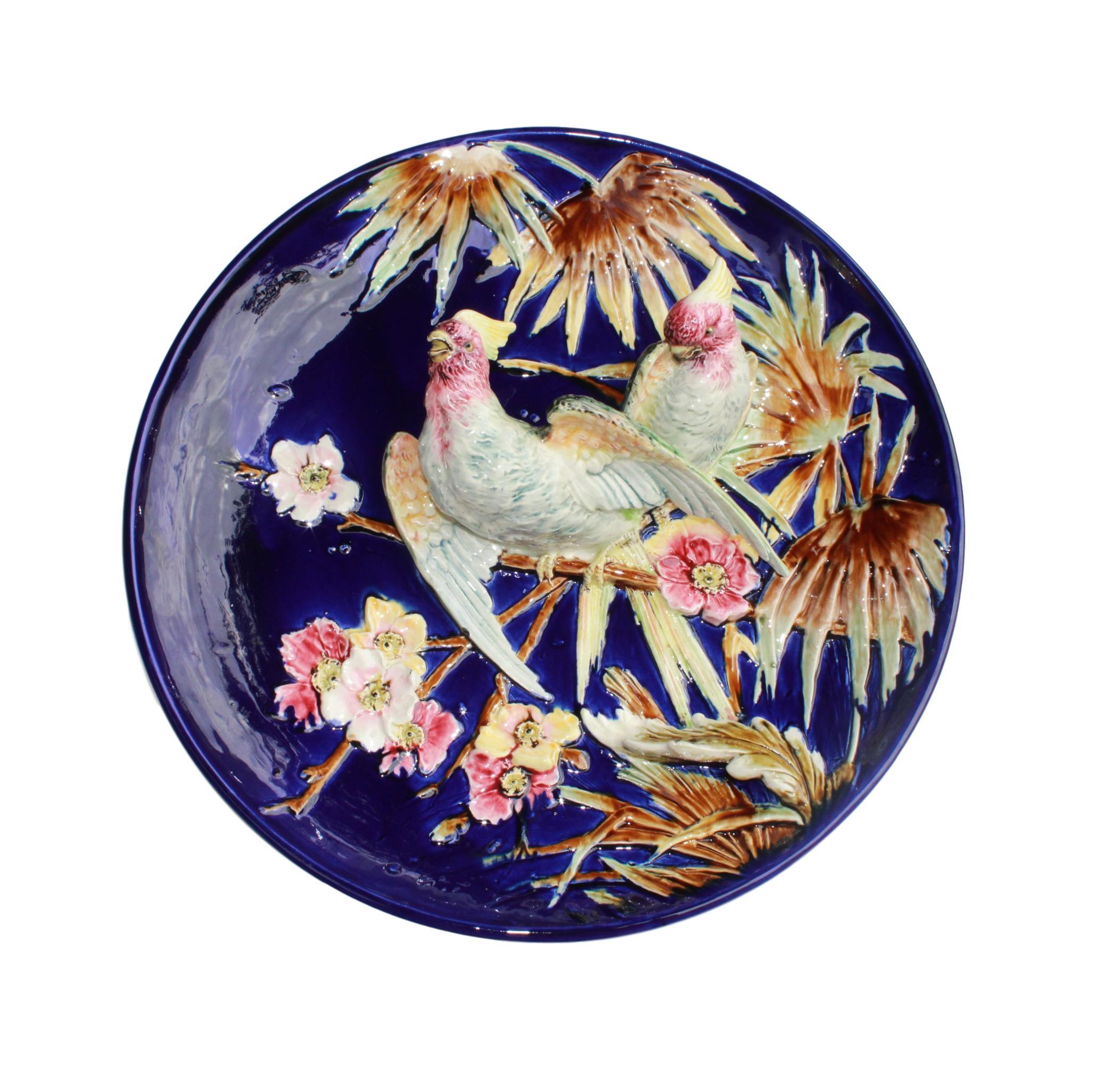 Very Large French Majolica (Barbotine) Trompe L'oeil Charger or plaque, with two naturalistically glazed cockatoos, molded in high relief among bamboo branches and flowers glazed in red, pink, and yellow, against a cobalt blue glazed ground, French,