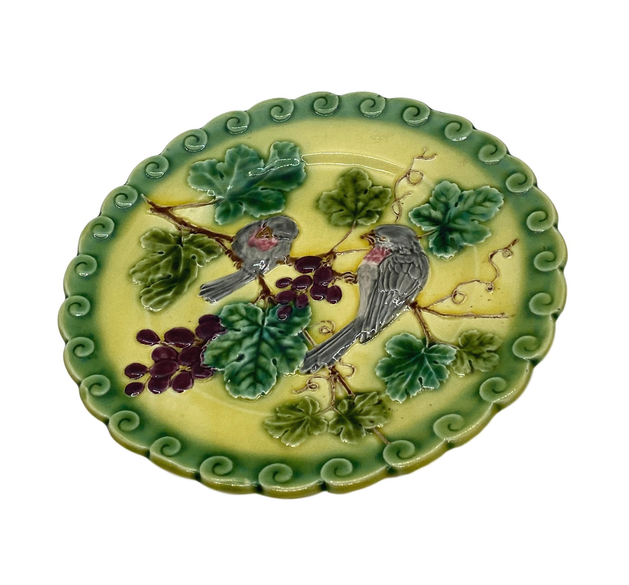French Majolica (Barbotine) Trompe L'oeil plate, with two relief molded pink sparrows among purple grapes and green glazed leafy vines, on a yellow glazed ground, with a stylized rolling wave, scalloped and green glazed border, the reverse with
