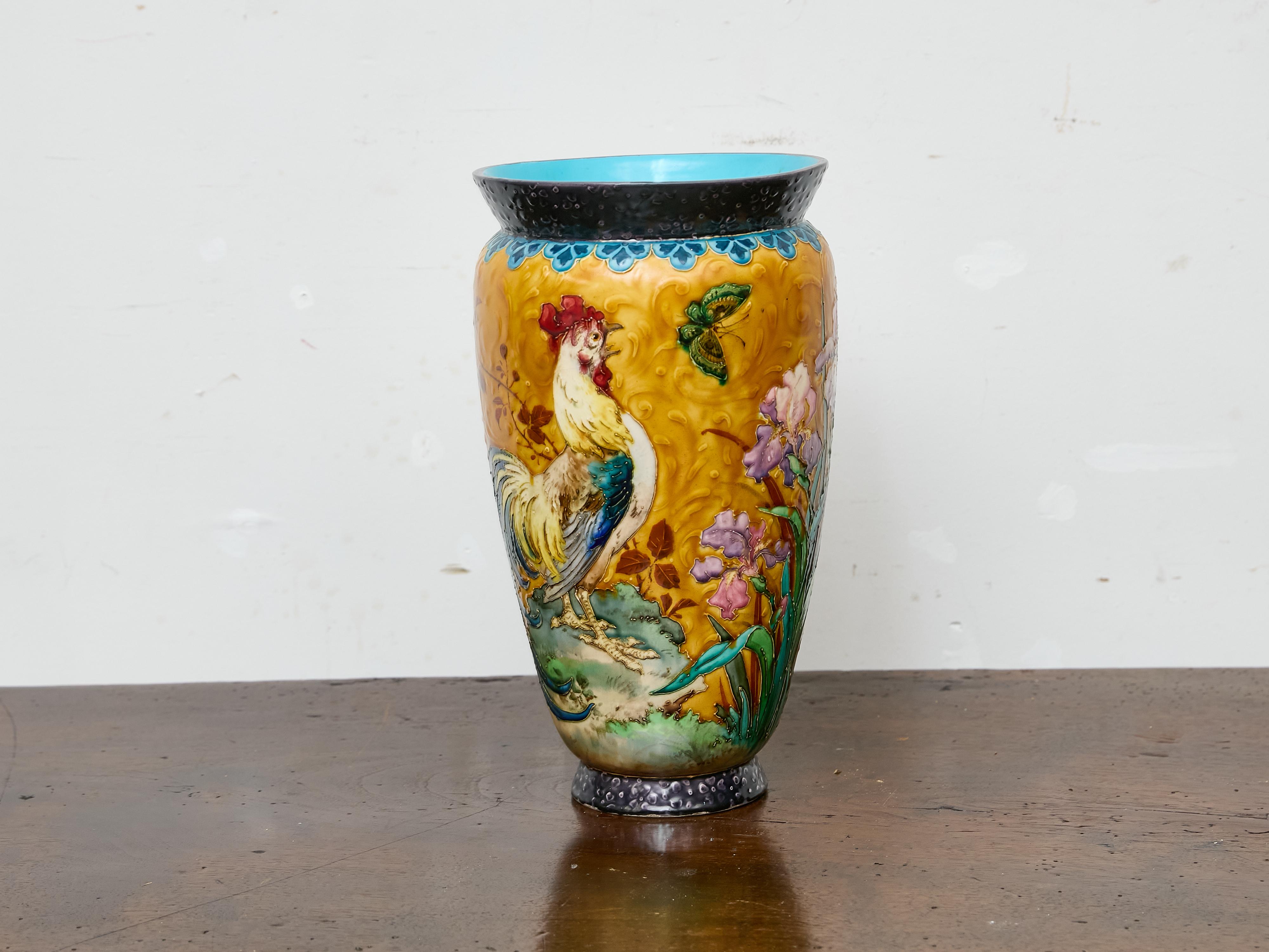 Ricco di colori e profondamente strutturato, questo vaso in maiolica francese risale al 1900 circa e presenta un suggestivo tableau di bellezza naturale. L'alta forma ovoidale è decorata in altorilievo con una scena vivace che raffigura un gallo