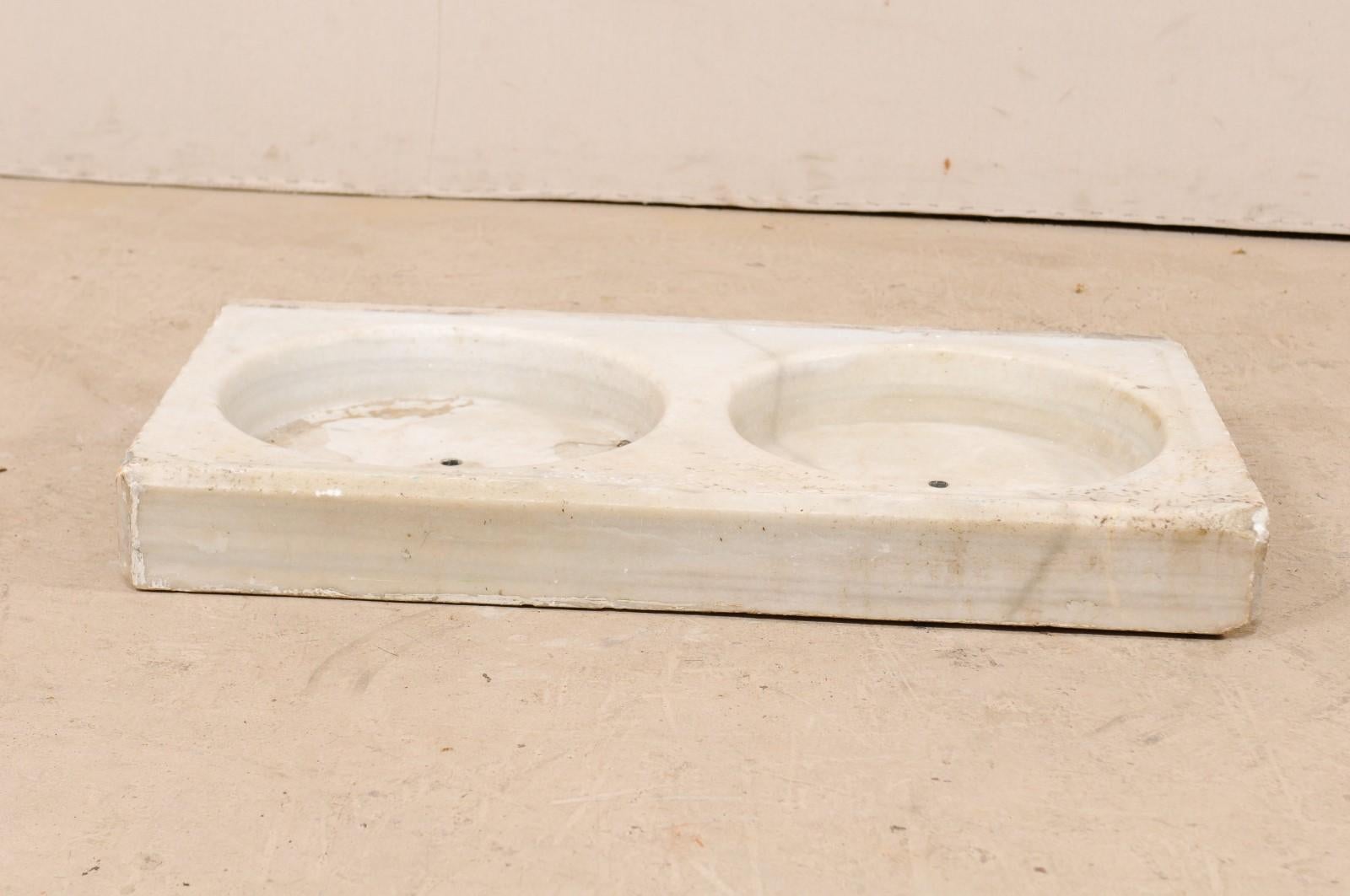 A French double basin sink of carved marble from the 19th century. This antique hand-carved marble sink from France has an overall rectangular-shape, and set with a pair of perfectly round, shallow basins. There is a small drain hole at the centre
