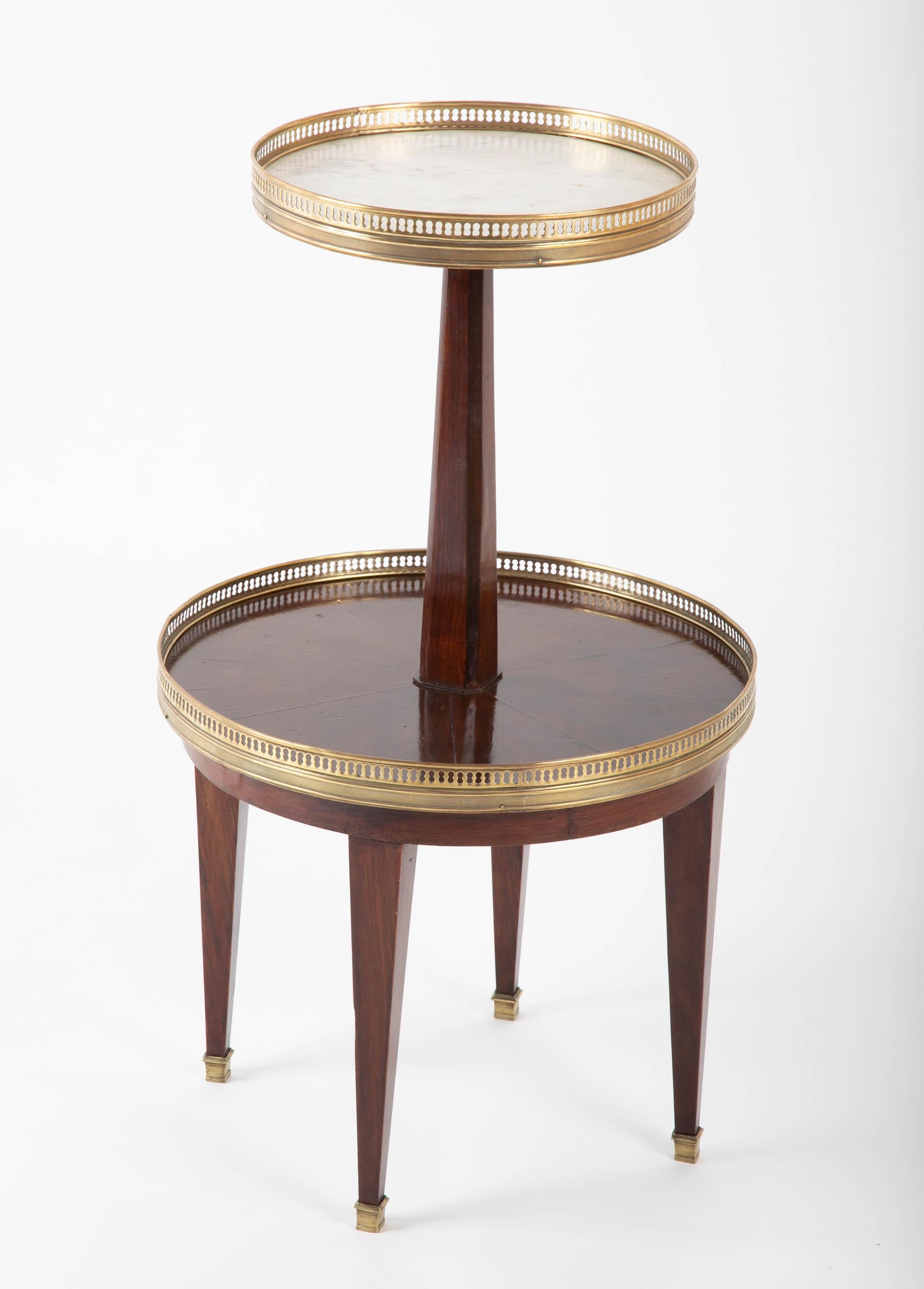 A charming and fine quality Louis XVI style two-tier dessert table, the top marble, the bottom mahogany, both with brass supported by four legs with brass sabot feet. France, last quarter of the 19th century. This notable side table or drinks table