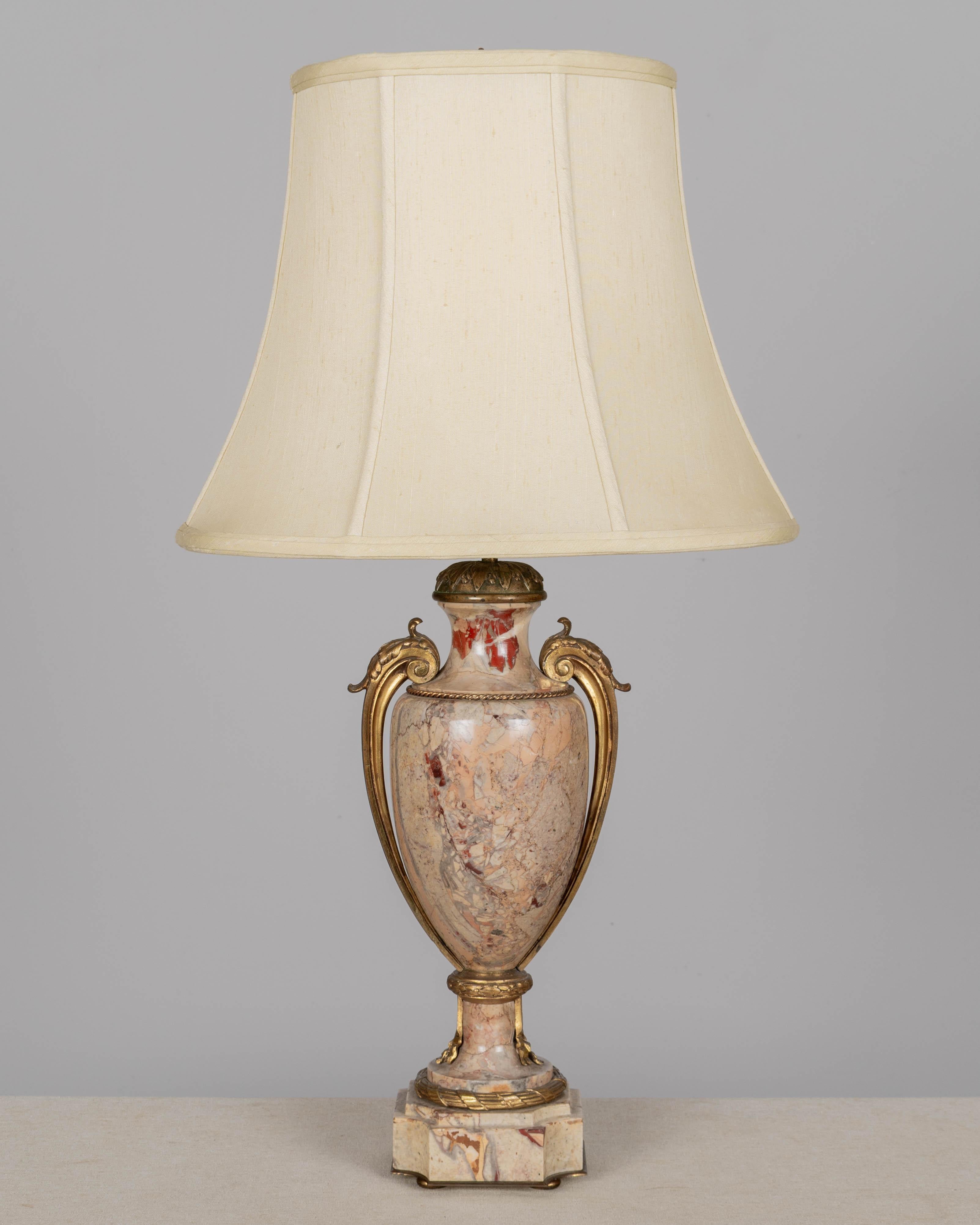 Lámpara de sobremesa de estilo Luis XVI con cuerpo en forma de urna de mármol y monturas de ormolu. Precioso mármol veteado gris, malva y burdeos. Las monturas ornamentadas de bronce fundido incluyen asas con volutas, un collar y motivos clásicos.