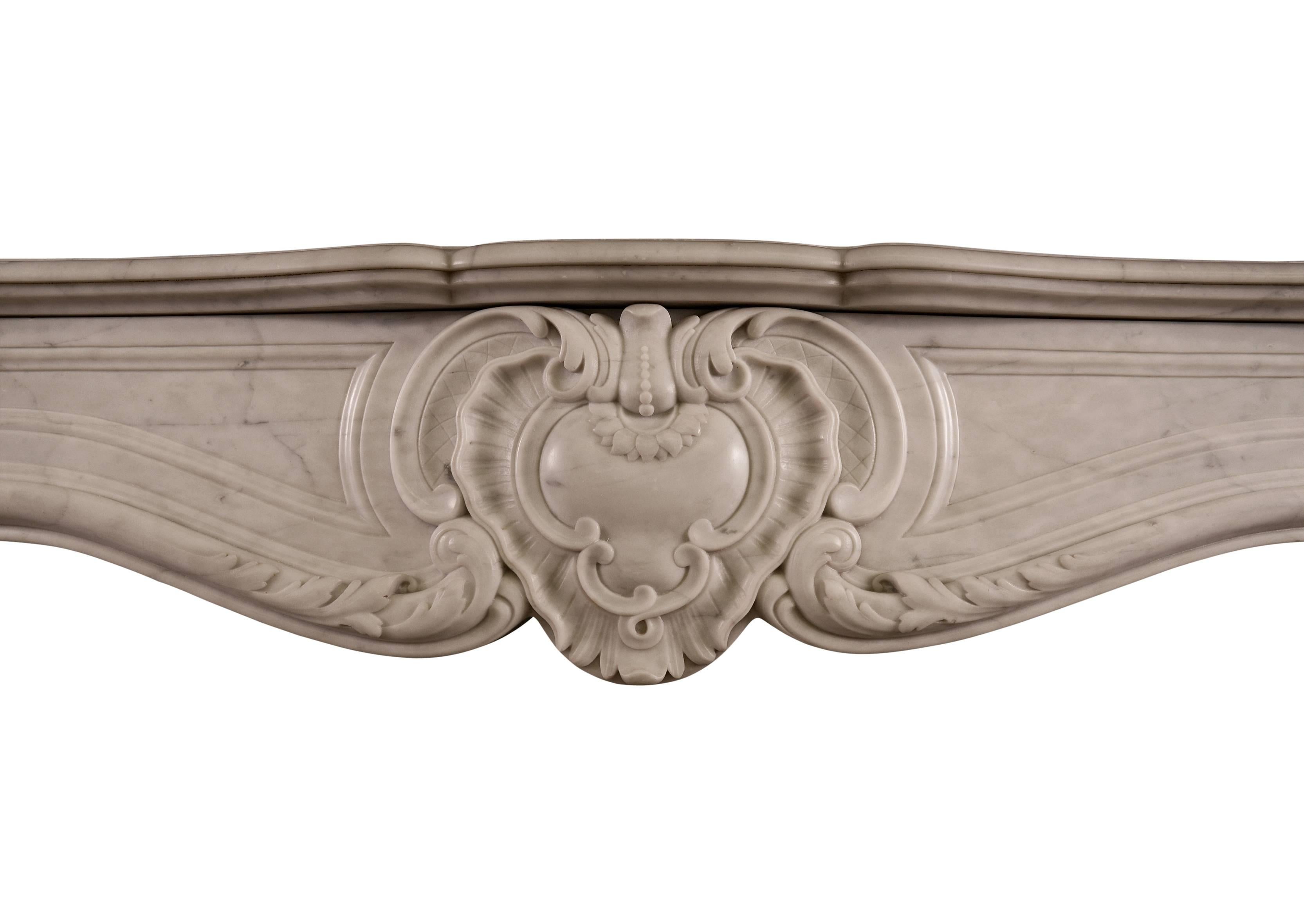 A French marble fireplace in the Louis XV manner. The shaped jambs with stiff acanthus leaves surmounted by carved bellflowers, scrollwork and foliage. The frieze with cartouche to centre flanked by foliage. Shaped moulded shelf above, French, 19th