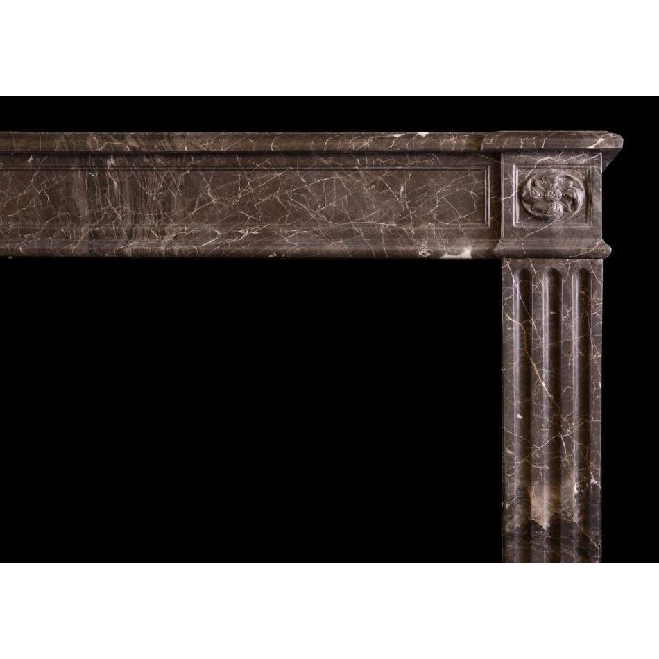 A French Louis XVI style fireplace in veined brown/grey marble. The stop fluted jambs surmounted by carved swirling paterae to end blocks. Panelled frieze surmounted by moulded shelf. A copy of an 18th century original.

Additional