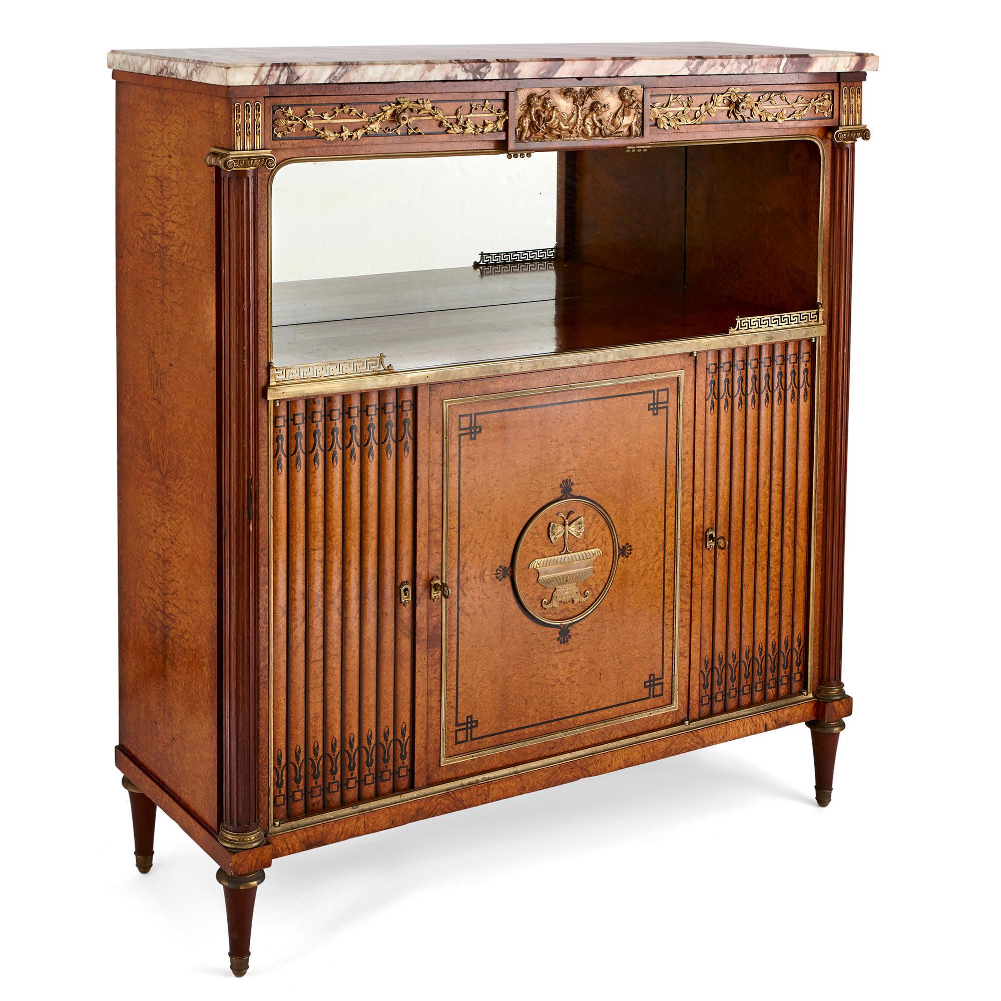 This wonderful side cabinet was created in France in the 19th century. The cabinet is crafted from amboyna burl wood, with inlaid ebony wood decoration and gilt bronze (ormolu) mounts.

The cabinet is covered by veined white marble. This tops a