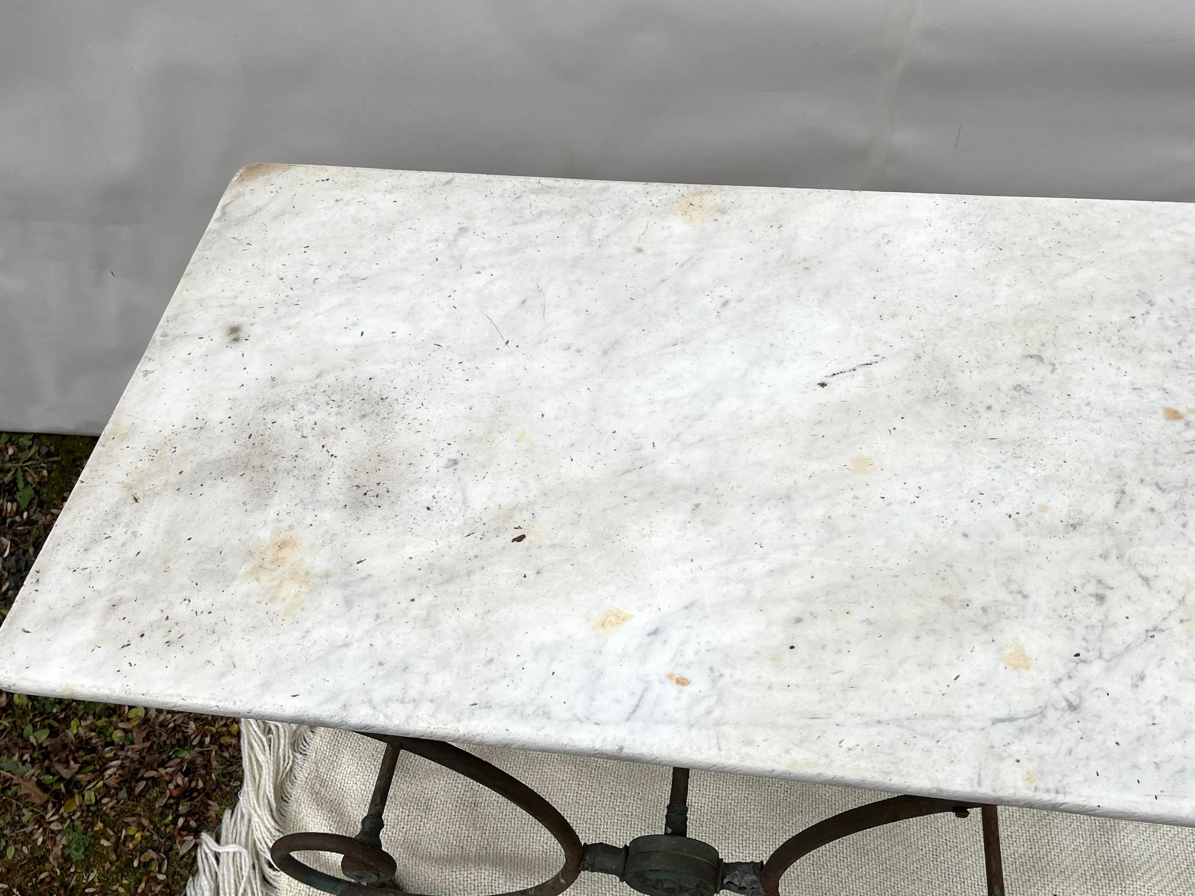 A 19th century French, wrought iron and white marble baker’s table circa 1870, weathered from being used outdoors, with patinated brass acorn finials and traces of old green paint. As the French say “dons son jus”.Tons of character. Would make a