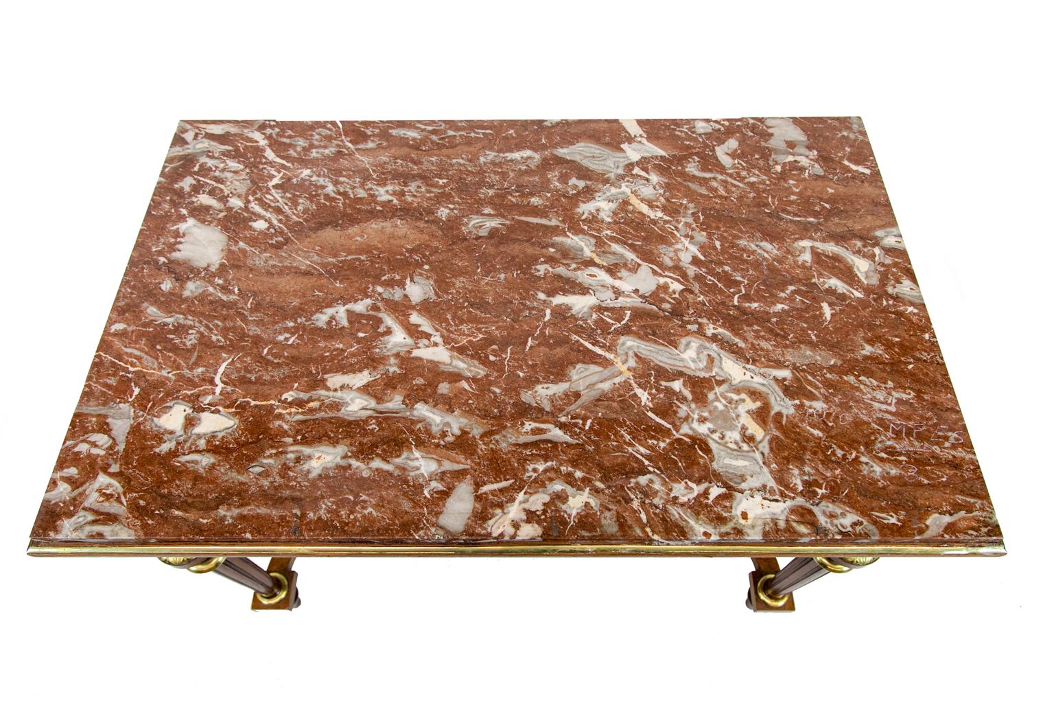 French marble top center table, with the marble having soft earth tones and is surrounded by a brass molded top. The base has brass molded panels and apron. Floral brass ornaments are on the fluted legs which have engraved brass leaf ornamentation.