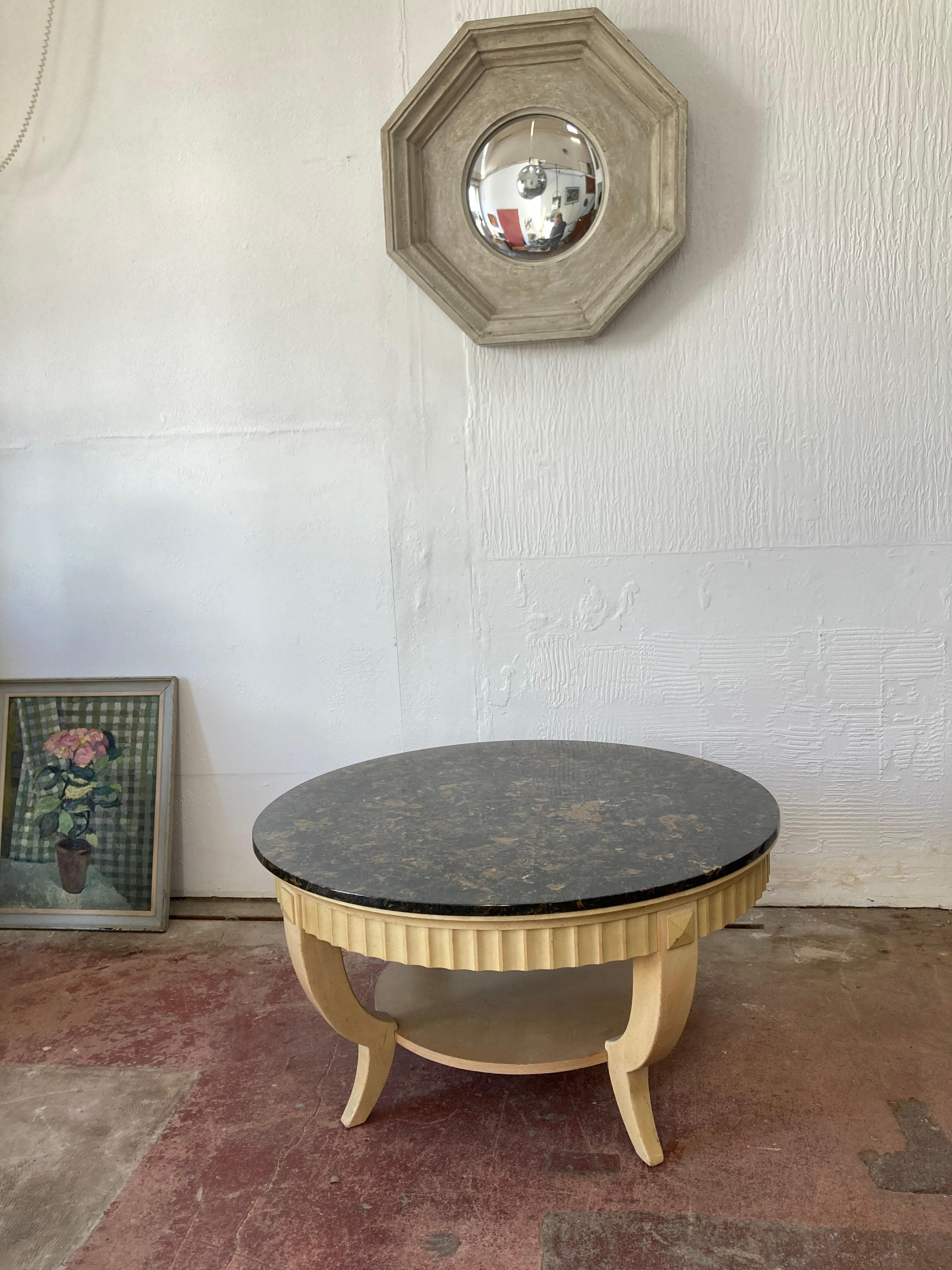 Superbe table basse circulaire, base en bois peint et sculpté à trois pieds avec un sous-bassement pratique, le plateau avec une bande cannelée qui supporte un grand plateau circulaire en marbre composite. 

Datant des années 1950, cette table
