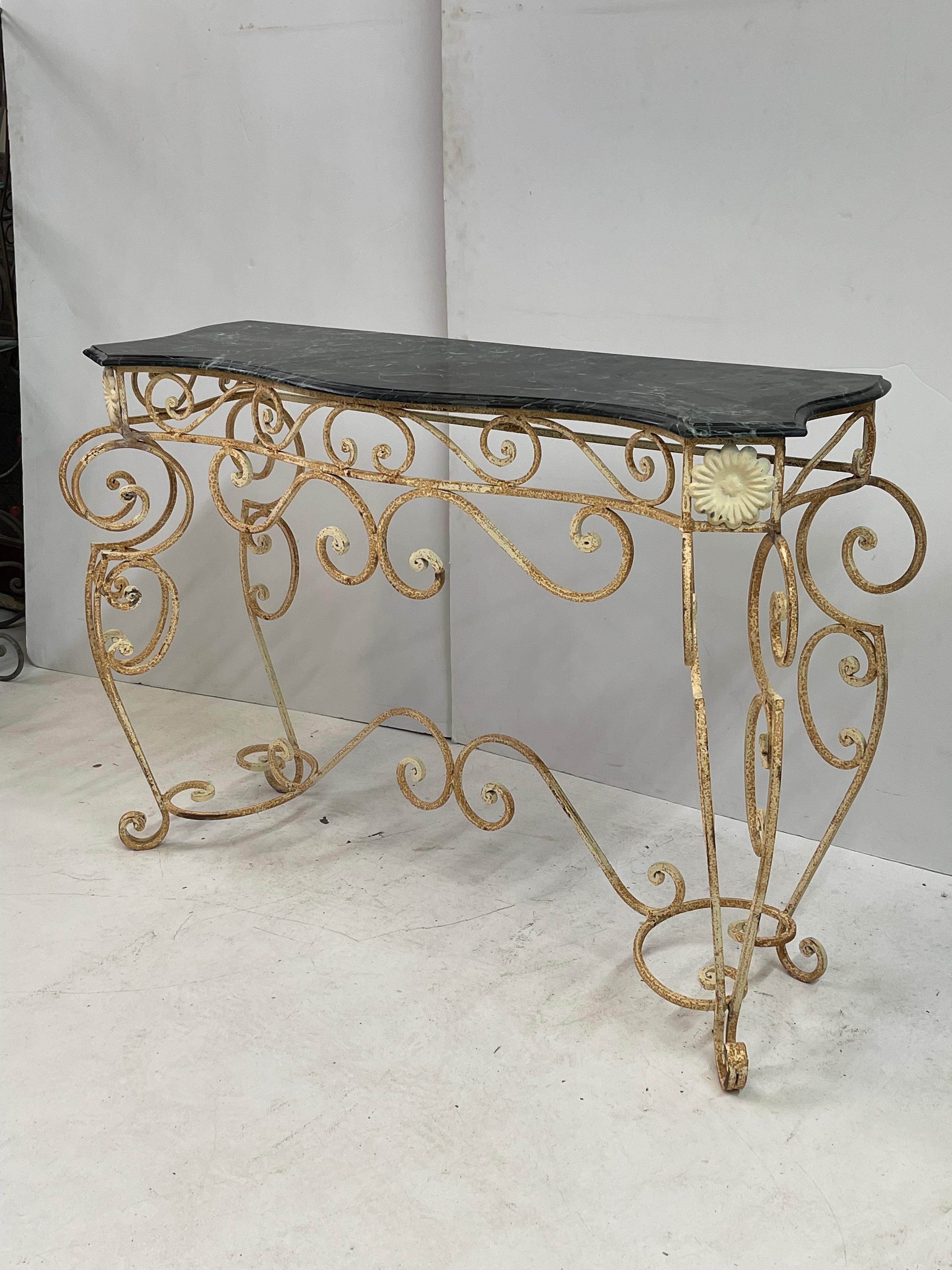 20th Century French serpentine shaped console table of scrolling iron. The table has a shaped and beveled top of dark green marble. The finish of the table base is cream paint on iron that has beautifully aged and oxidized over time. 

The table