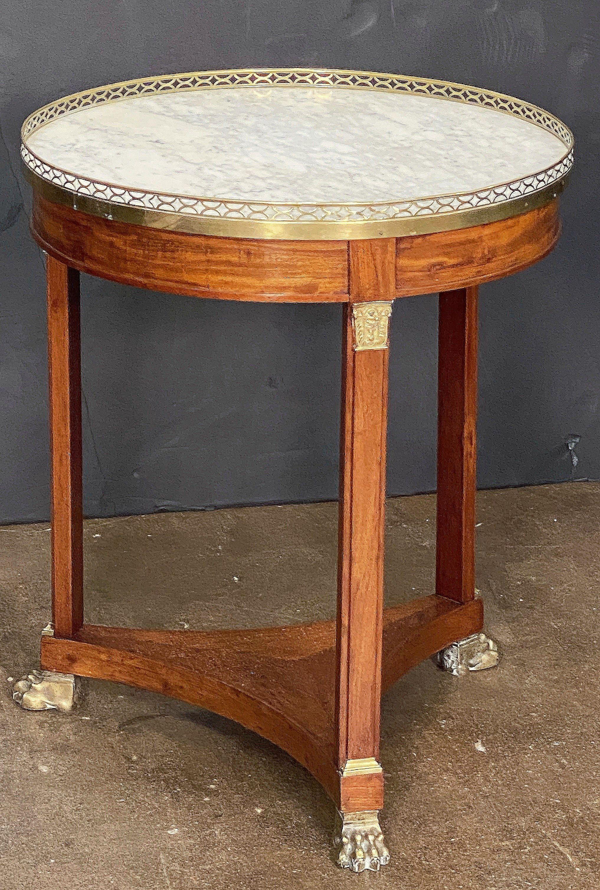 Bellissimo tavolino francese rotondo o gueridon in stile Impero, con piano circolare in marmo bianco figurato circondato da una galleria bassa in ottone traforato, posto su un supporto a colonna tripode in noce patinato con finiture decorative in