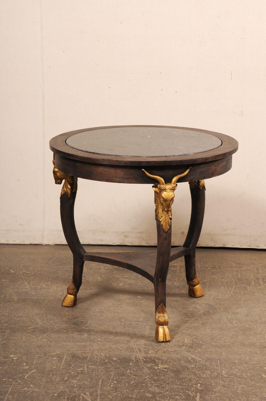 A French vintage round occasional table with marble top and goat head accents. This smaller-sized table from France features a round-shaped top, fitted with recessed marble within its center (leaving a nice, thick band of wood about the perimeter),
