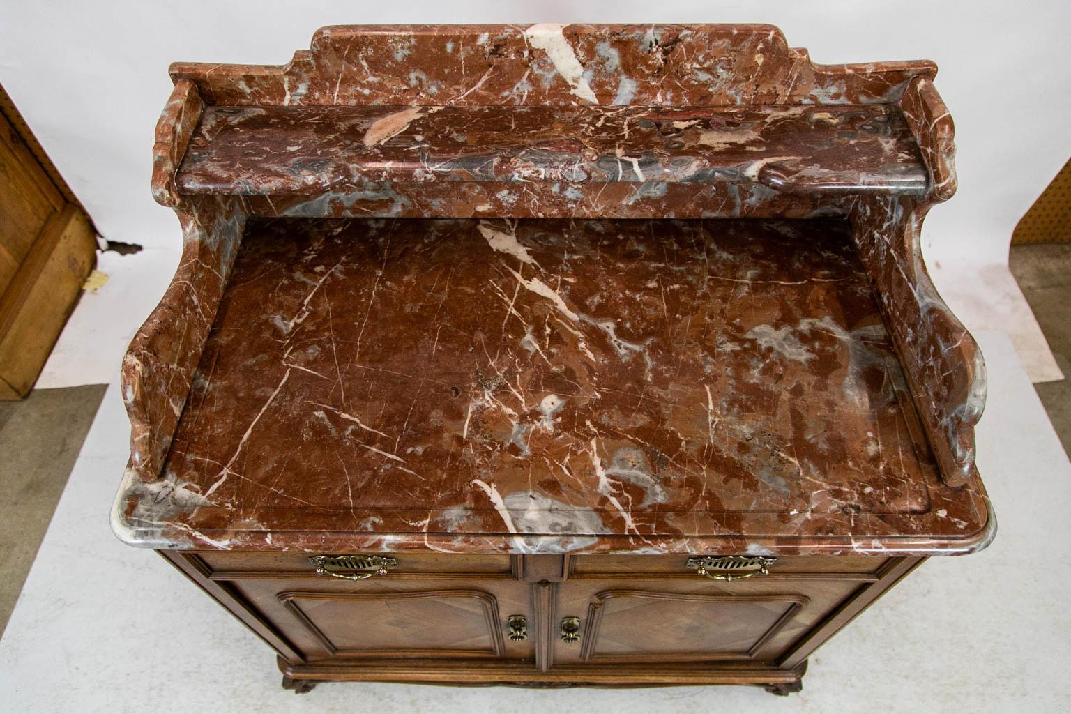 The doors and drawers of this washstand have bookmatched veneers framed with carved moldings. The sides have bookmatched herringbone veneers. The corners are carved and molded and terminate in stylized acanthus leaf feet. The marble top is shaped