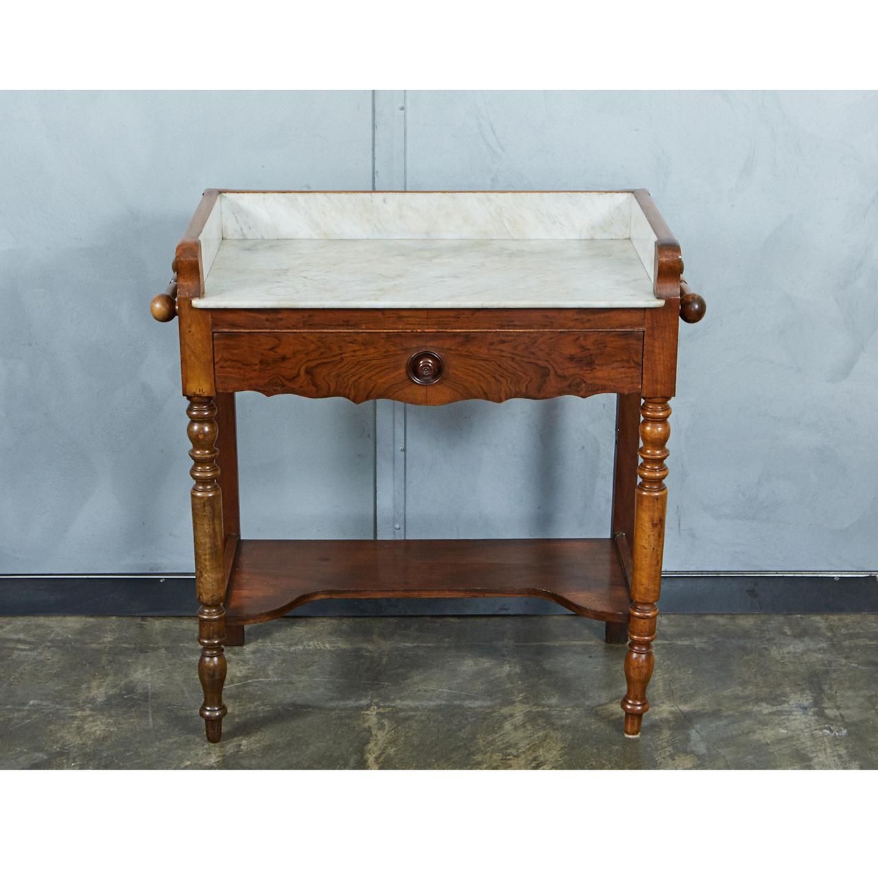 This diminutive French washstand is made from walnut with a marble top and gallery. The piece has a drawer with turned knob and divider. The piece has four turned legs, two turned handles at the sides and a small shaped shelf. We can picture this