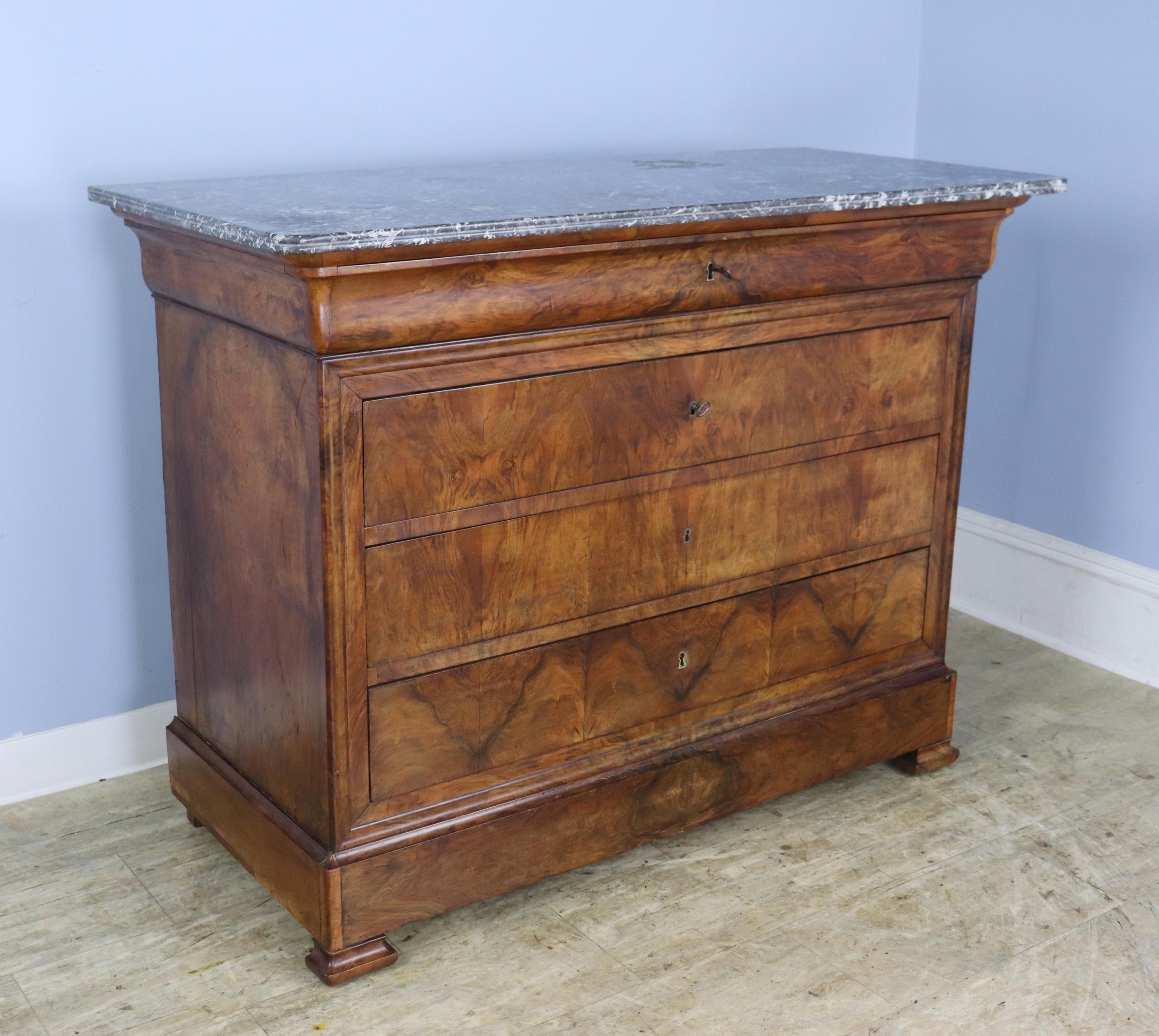 A classic Louis Philippe commode in dramatically grained walnut veneer.  Three wide drawers plus an extra hidden drawer in the top molding!  The book matched walnut has very good color and patina, and the marble is in moderate condition, with a